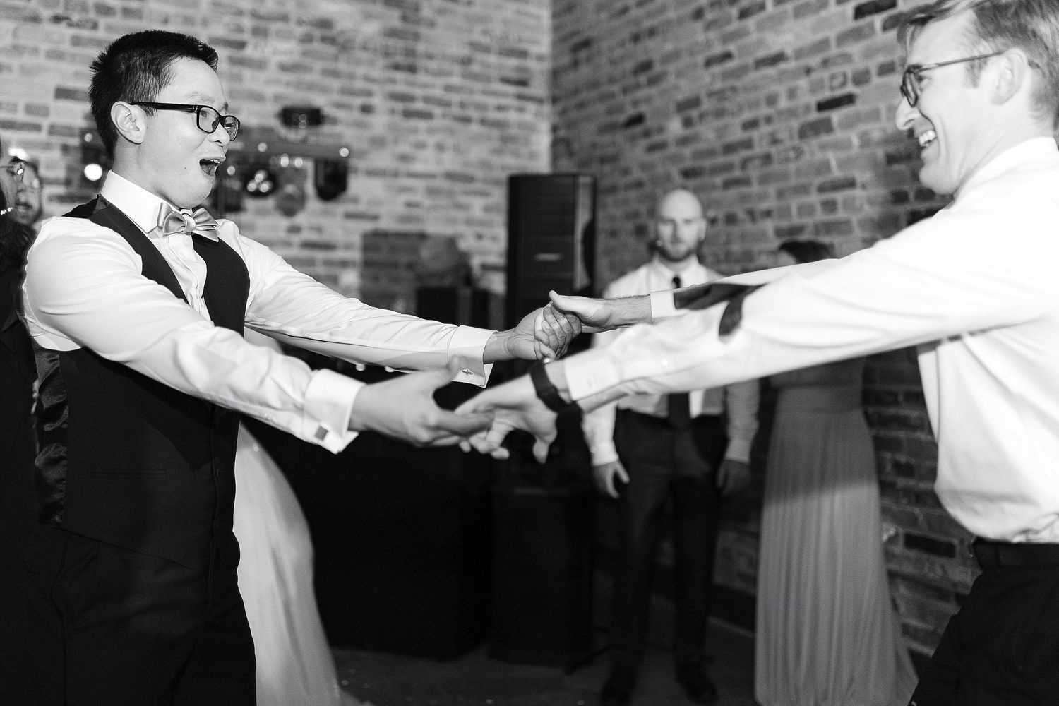 People swing dance in a vintage black and white photo against a brick wall background.