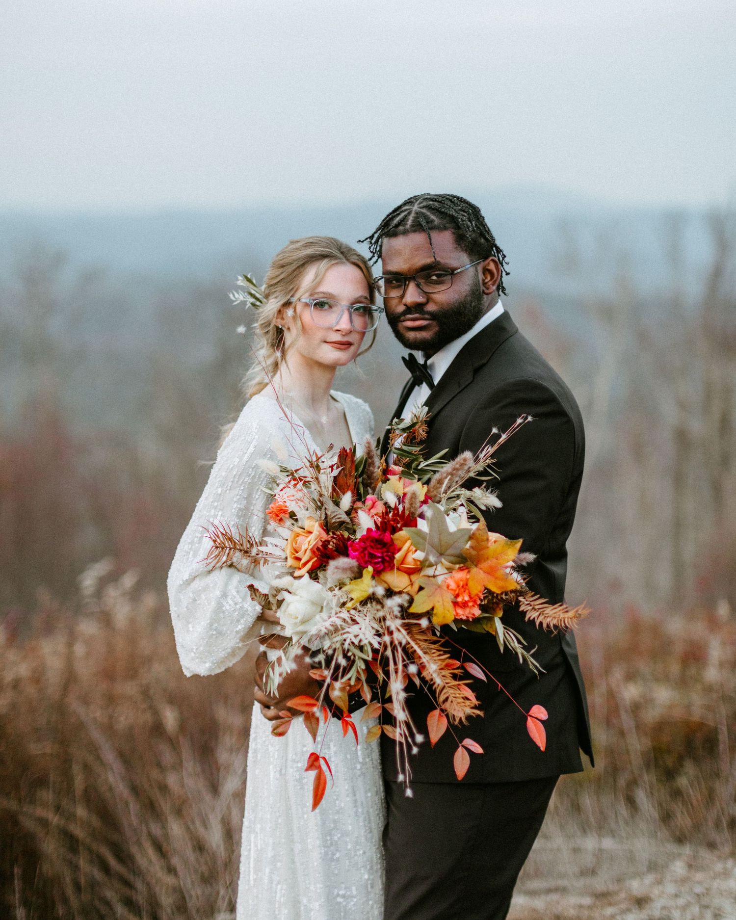 Intimate wedding portrait featuring elegant attire and a stunning fall-inspired floral arrangement.