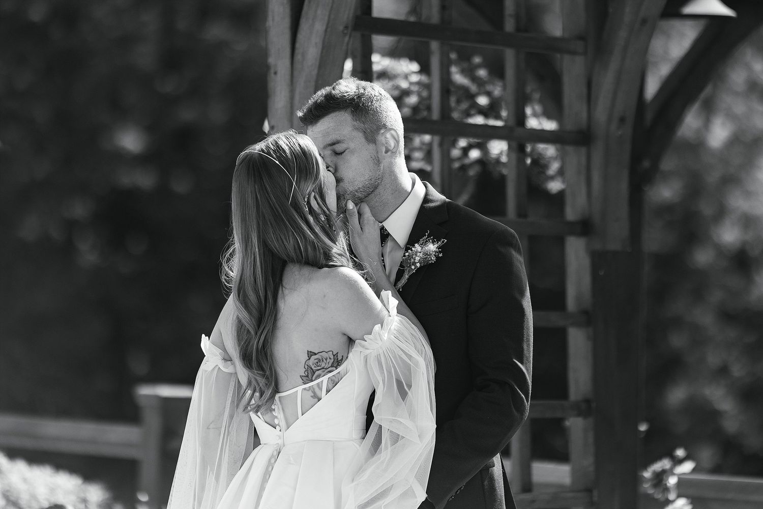 Black and white romantic moment captured under a wooden pergola.