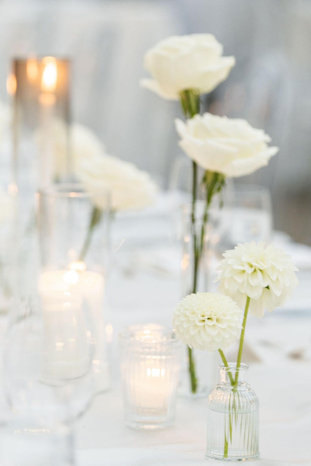 Delicate white flowers in glass vases with glowing candles create an ethereal table setting.