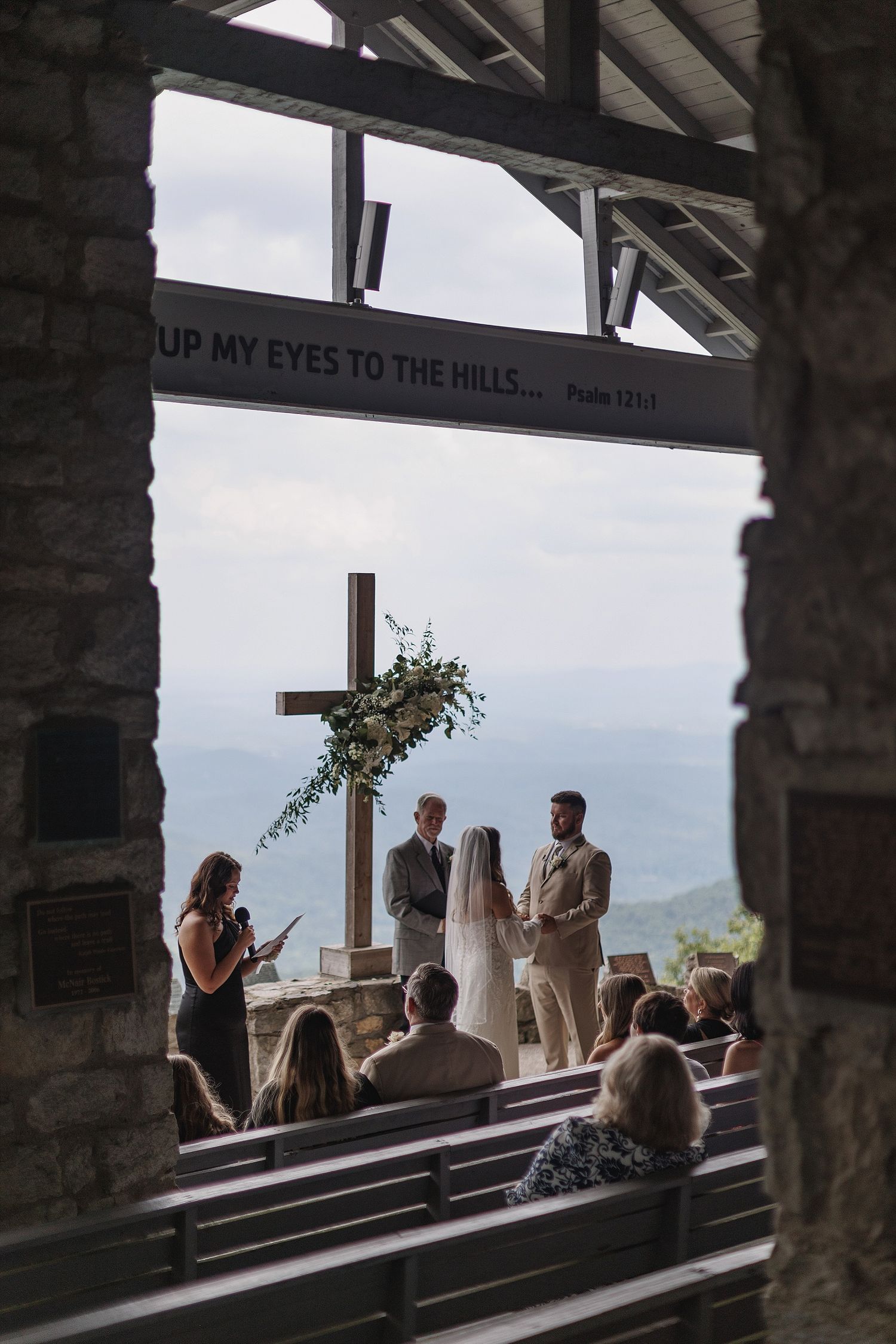 An intimate wedding ceremony in a rustic mountain chapel with a cross and scenic overlook.