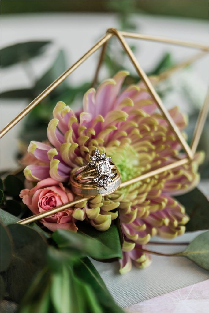 Wedding ring displayed in geometric gold frame with pink and green florals.