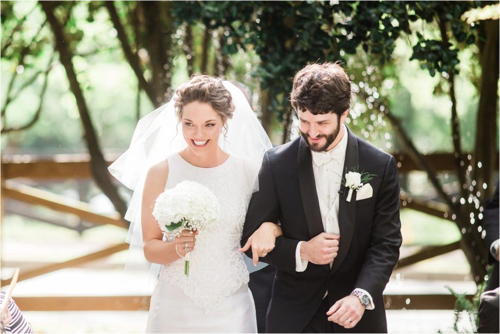 Joyful newlyweds walking together after ceremony with bride holding white bouquet.
