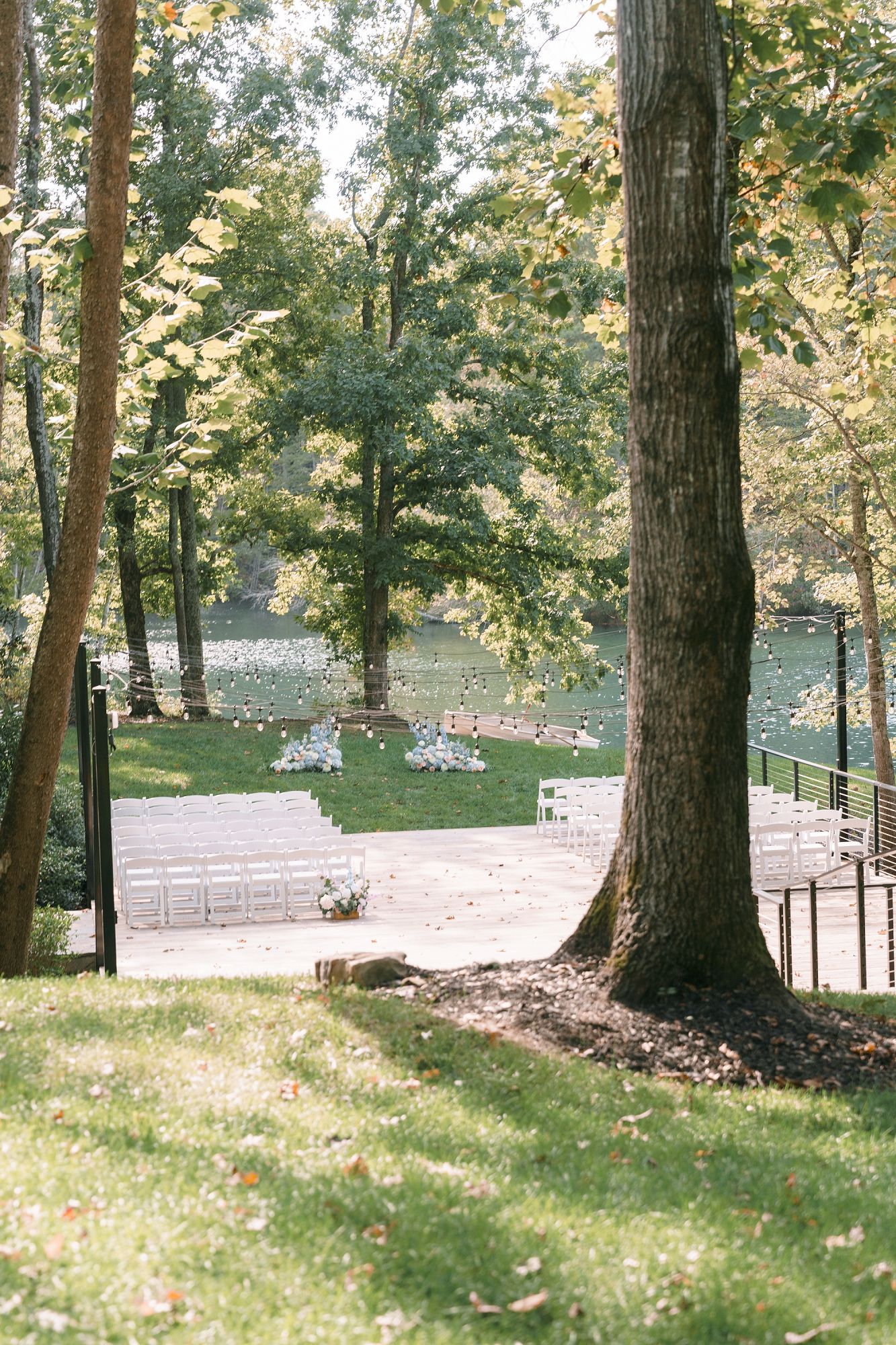 Outdoor wedding ceremony setup with white chairs arranged on a lawn surrounded by lush trees near a serene pond.