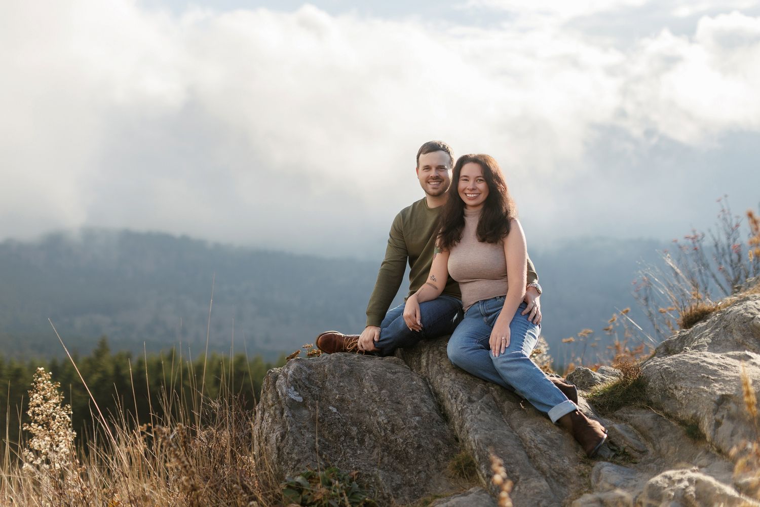 Two people sitting together on a rocky mountain overlook enjoying scenic mountain views in the distance.