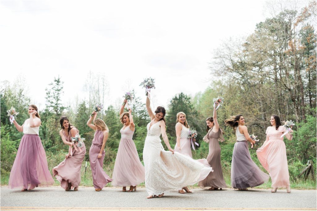 Bridal party in pastel dresses jumping joyfully on a country road.