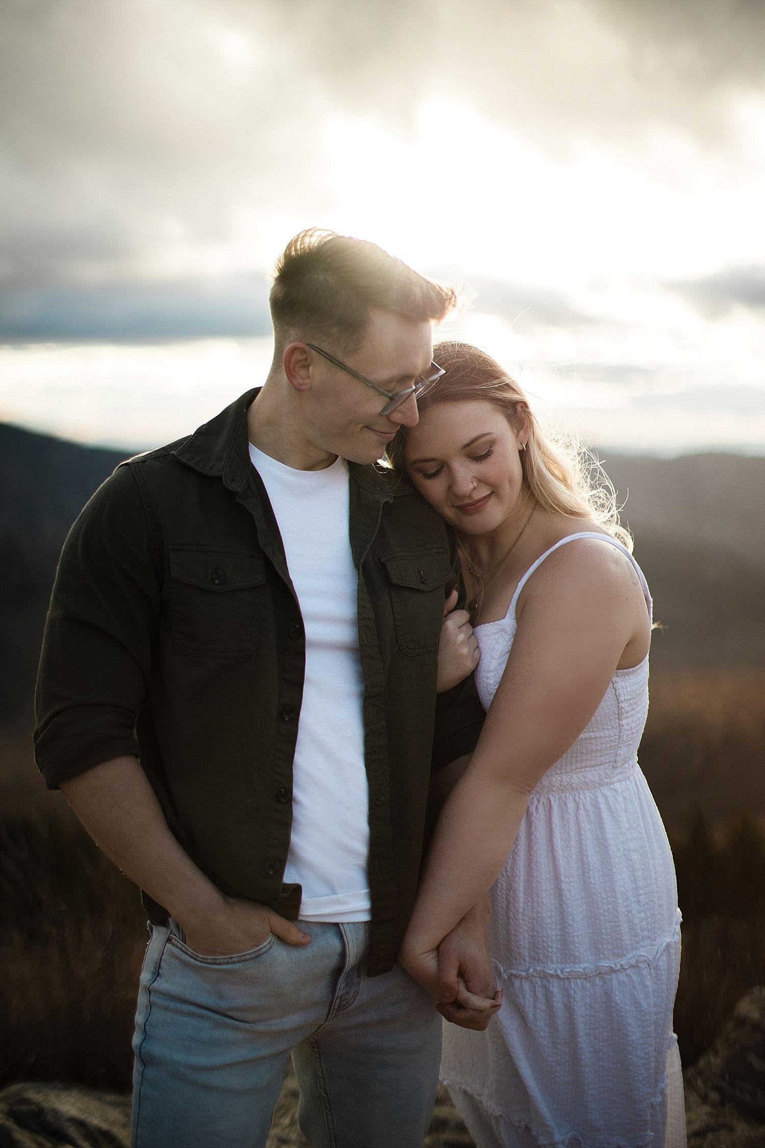 Golden hour engagement photo of a couple holding hands and resting their heads on each other