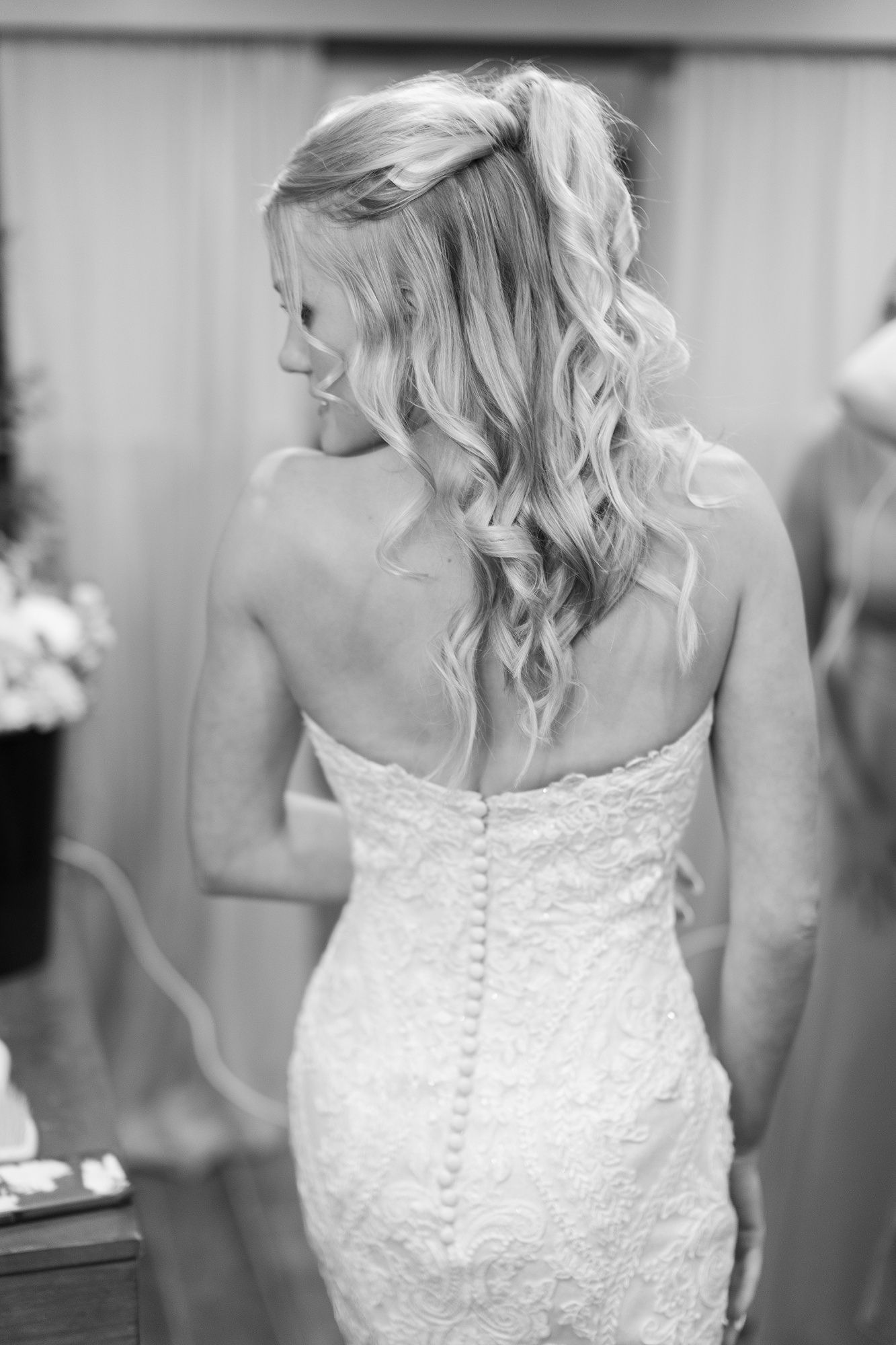 Bride in strapless lace wedding gown with long curled blonde hair viewed from behind.