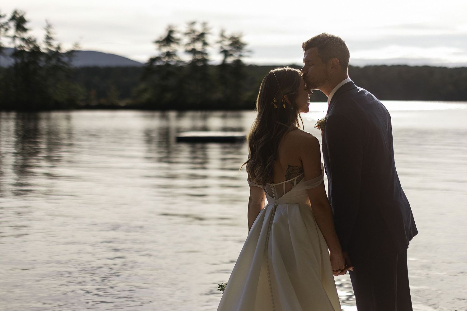 A romantic silhouette of a wedding couple by a serene lake at sunset.