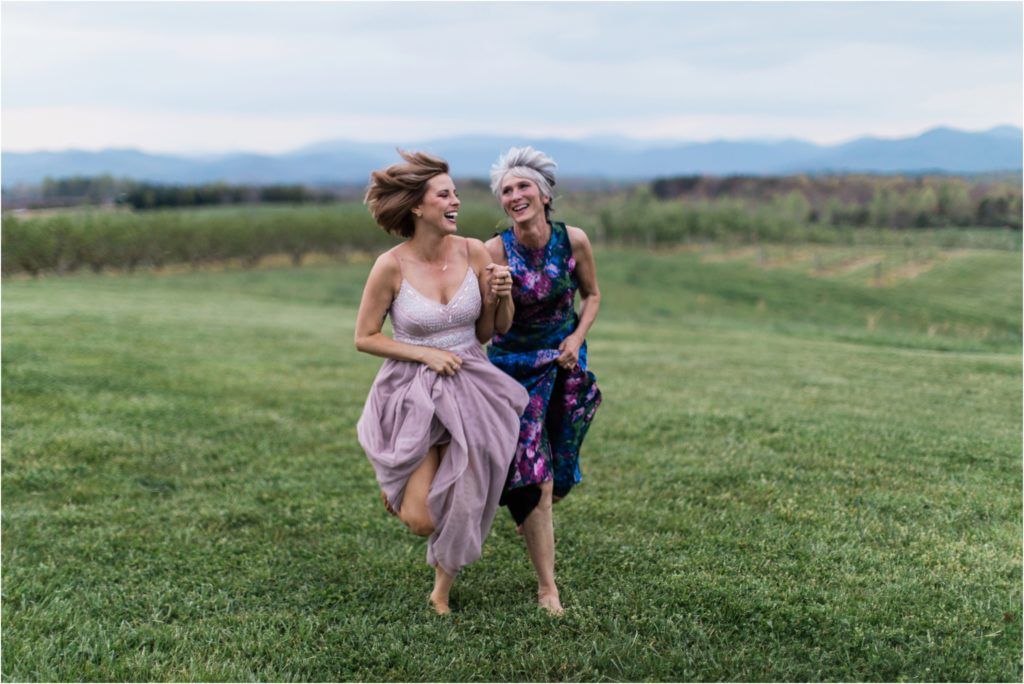 Two people running joyfully through a grassy field with mountains in the background.