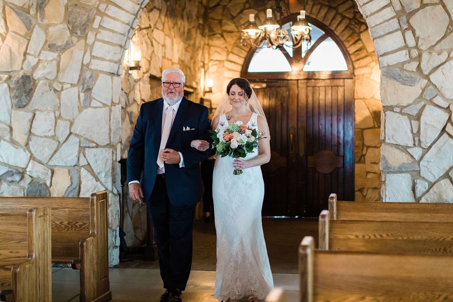 A processional moment inside a rustic stone chapel with wooden pews and arched doorway.
