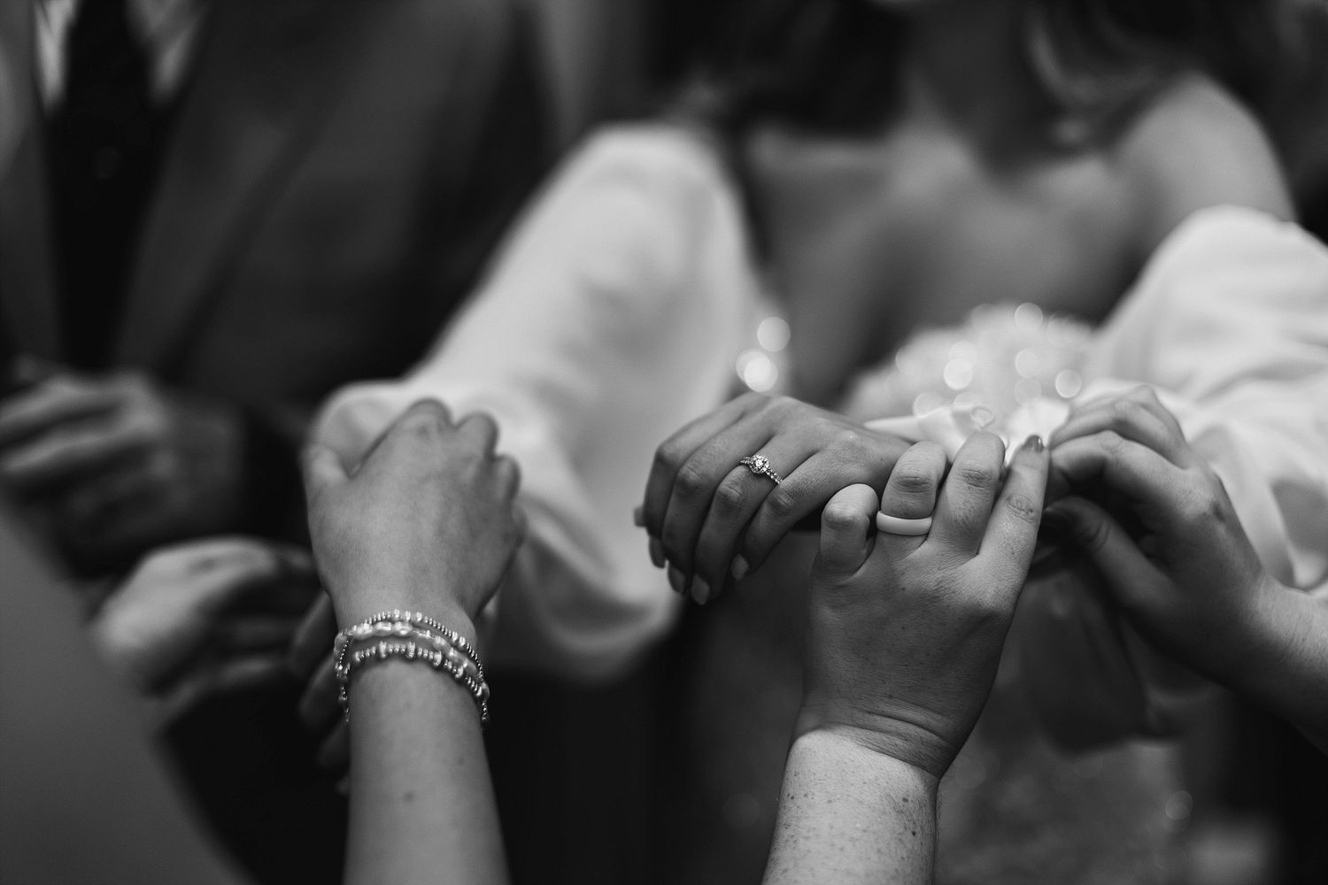 Close-up black and white shot of hands clasped together wearing rings and bracelets.