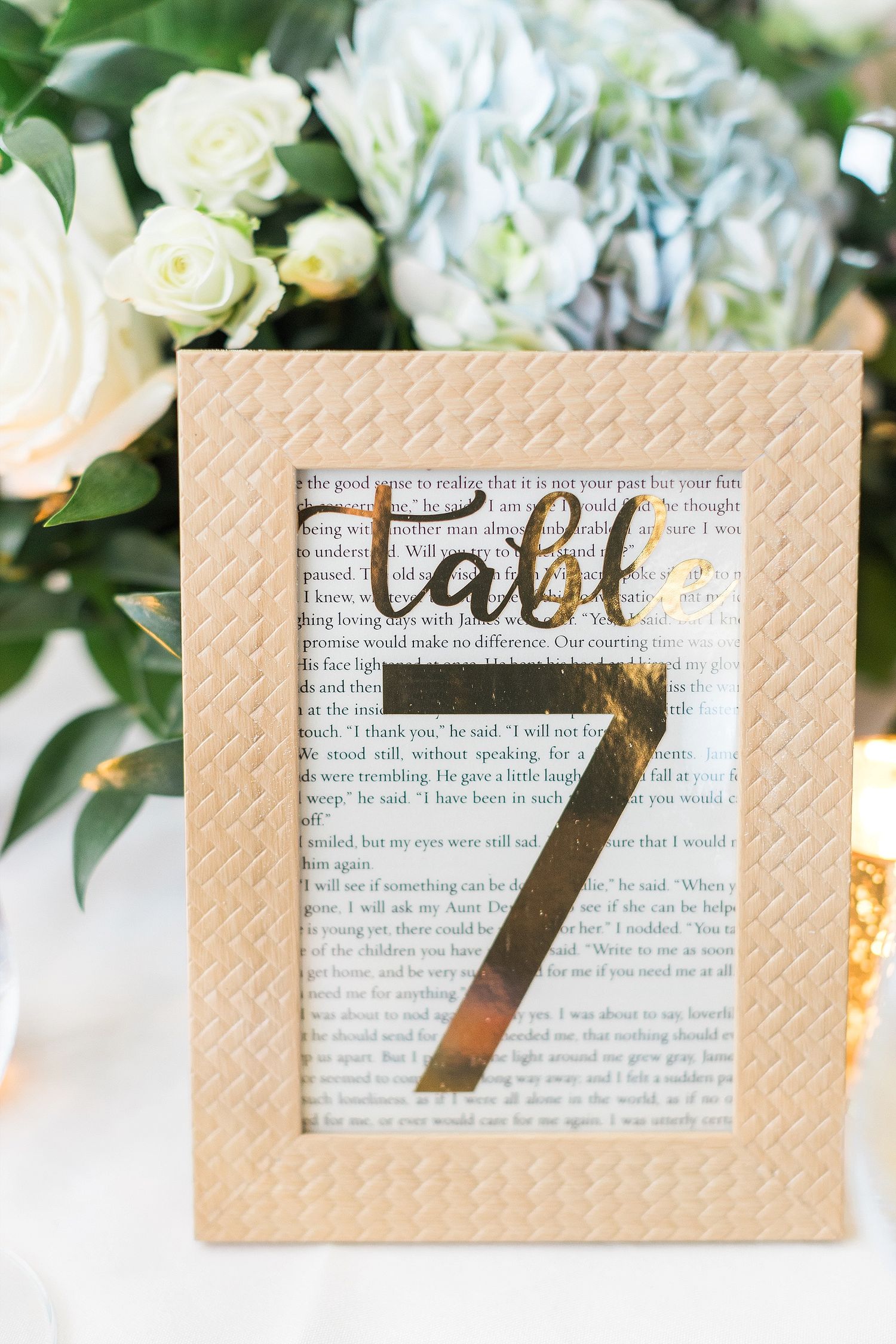 Table number display with gold metallic number on book page background in wooden frame.