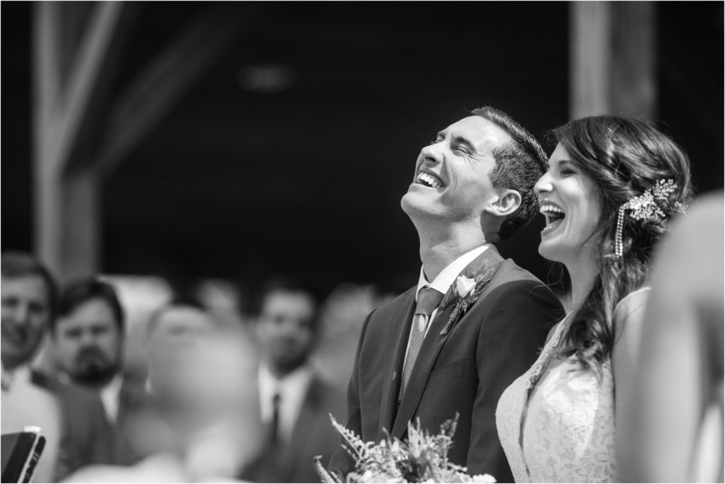Black and white candid photo of newlyweds sharing genuine laughter during ceremony.