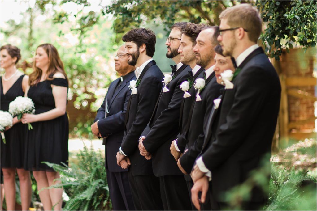 Wedding party in formal attire standing in garden setting.
