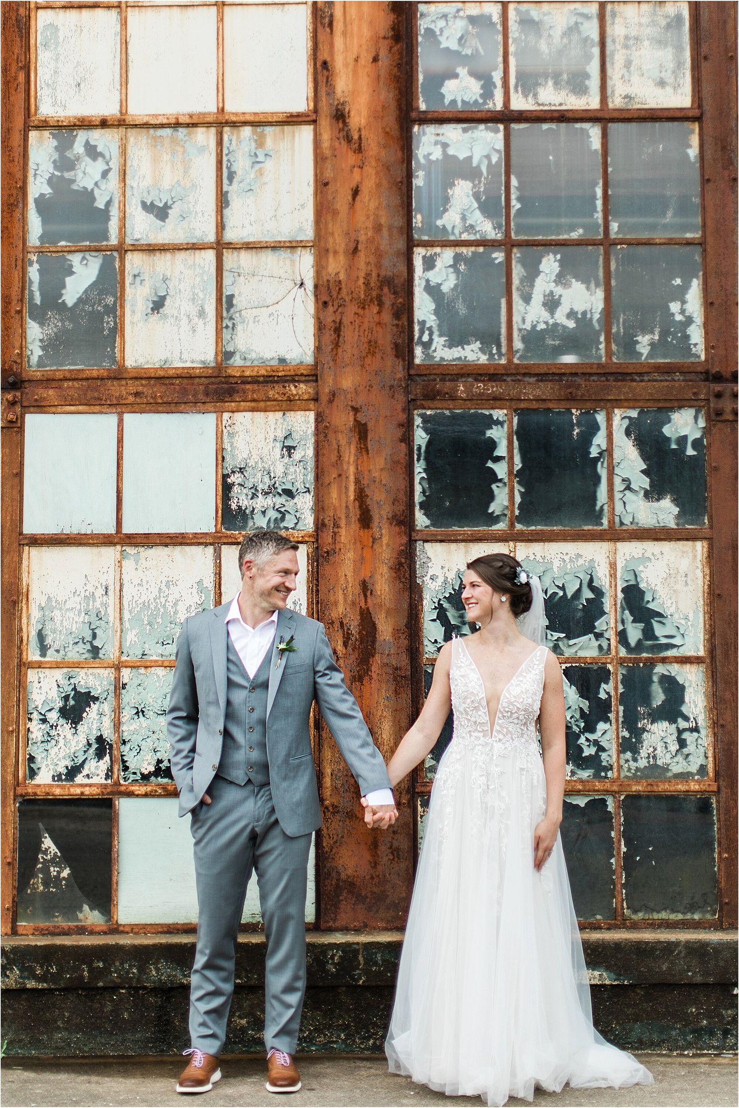 Newlyweds share tender moment in front of distressed factory windows.