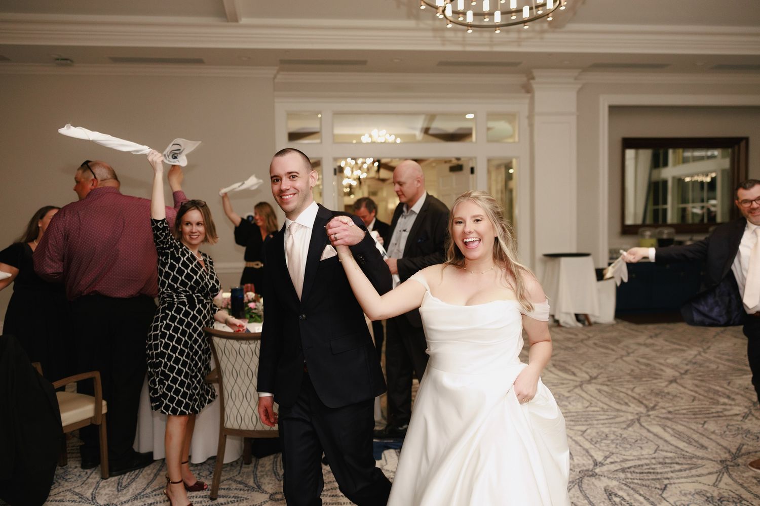 Wedding reception guests dancing and celebrating in an elegant ballroom with crystal chandeliers.