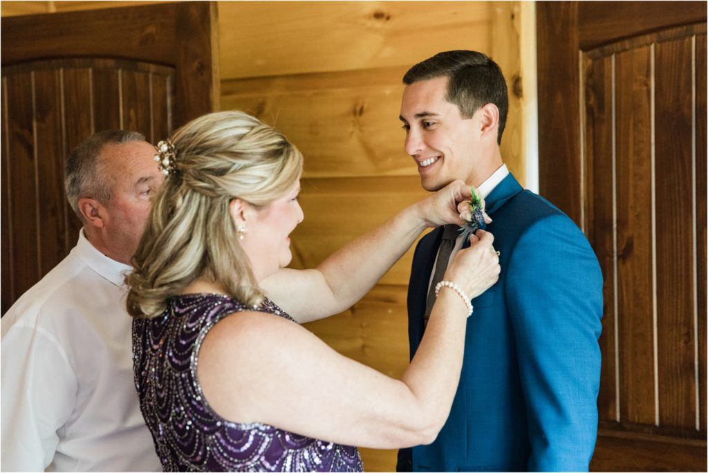 A woman in a navy dress helps adjust a bow tie on a man wearing a blue suit.