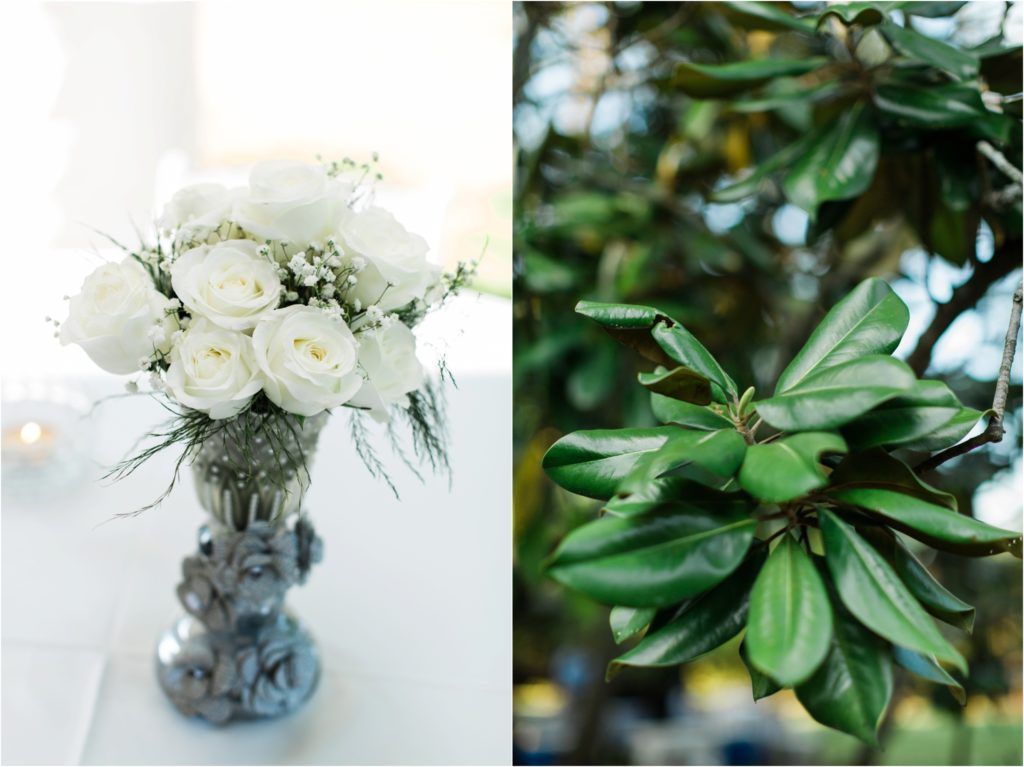 White roses in crystal vase next to close-up of glossy green magnolia leaves.