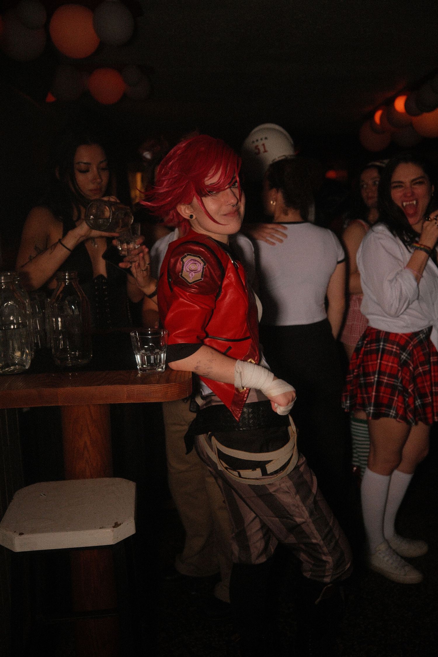 Person in red wig and costume dancing energetically at a party with friends in background.