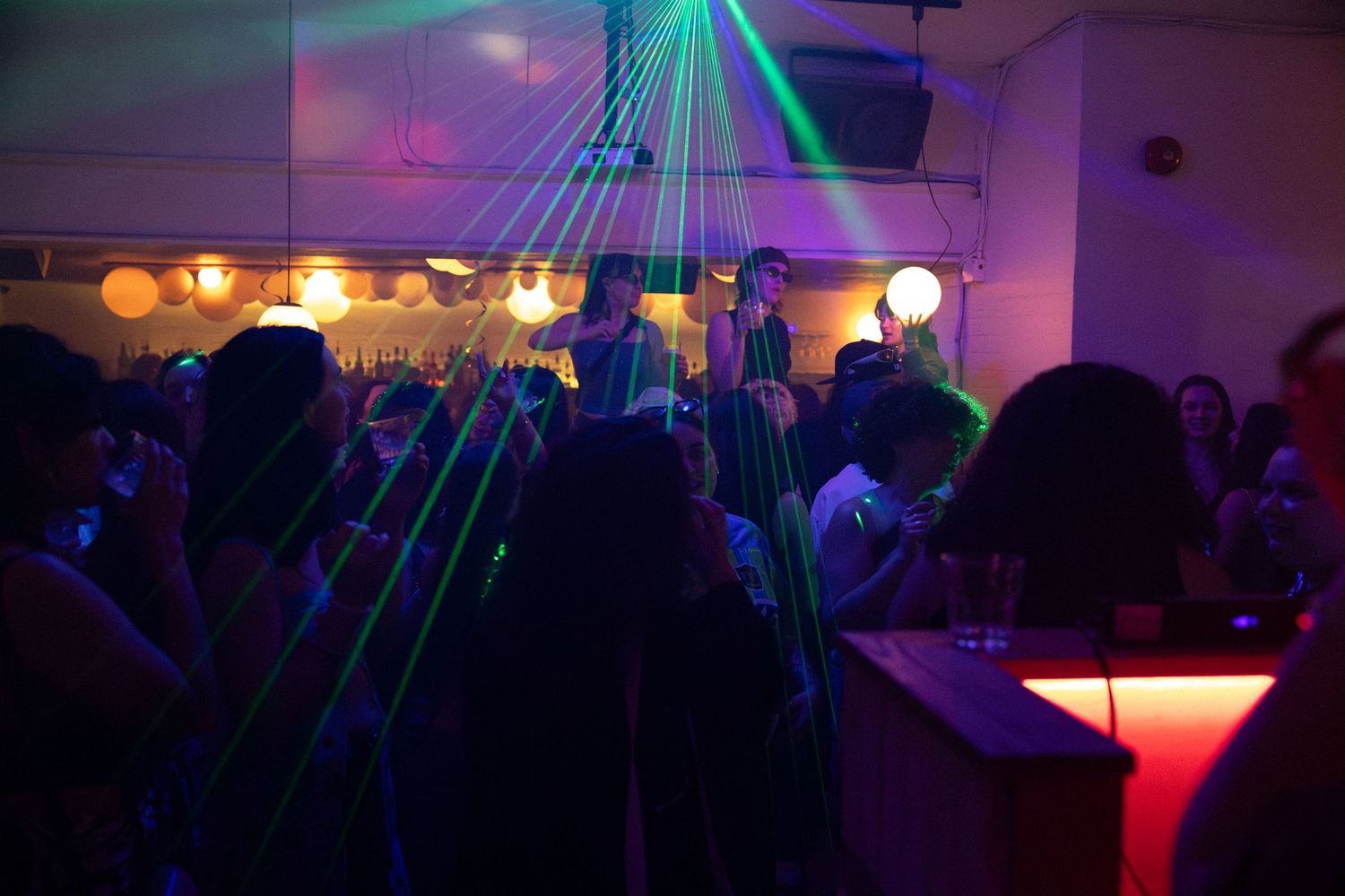 Crowd dancing under colorful laser lights at a vibrant nightclub party.