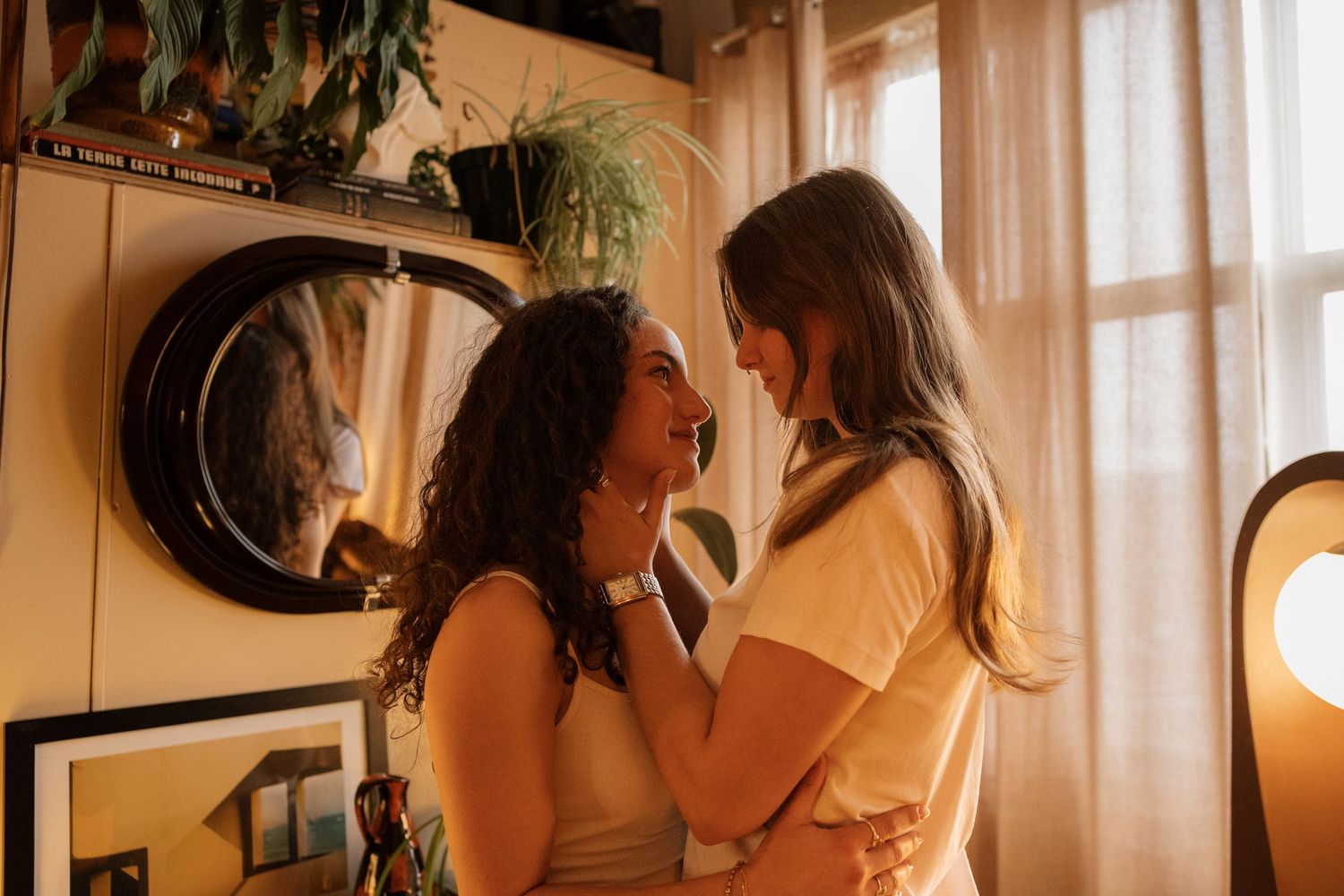 Two women share a tender moment embracing face-to-face in a warmly lit cozy room.