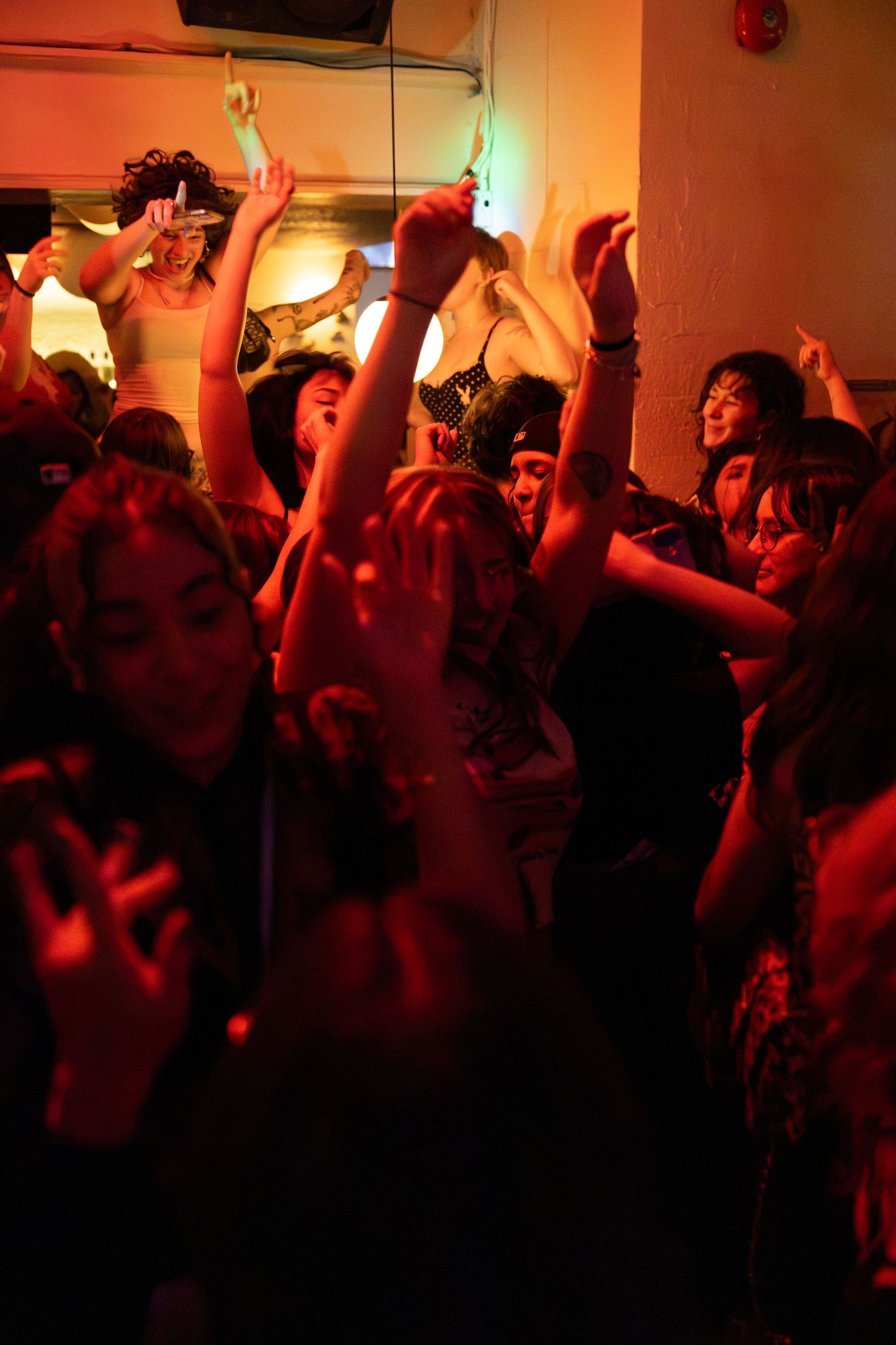 Energetic crowd dancing under warm orange lights at a packed indoor party or nightclub event.