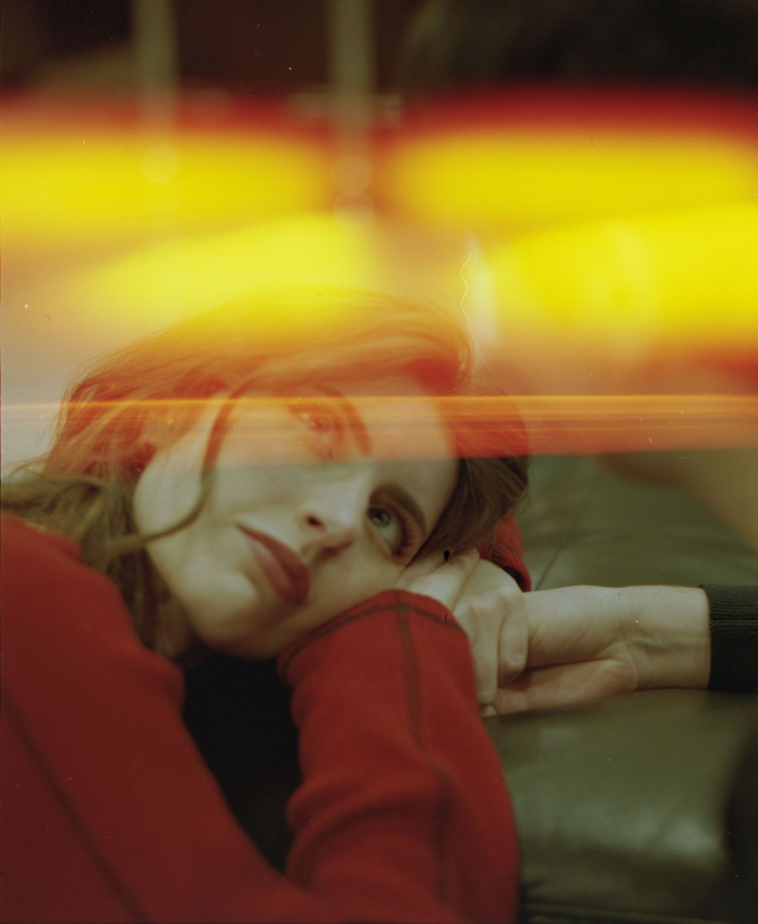 A woman in a red sweater rests her head on her arms, surrounded by colorful light streaks.