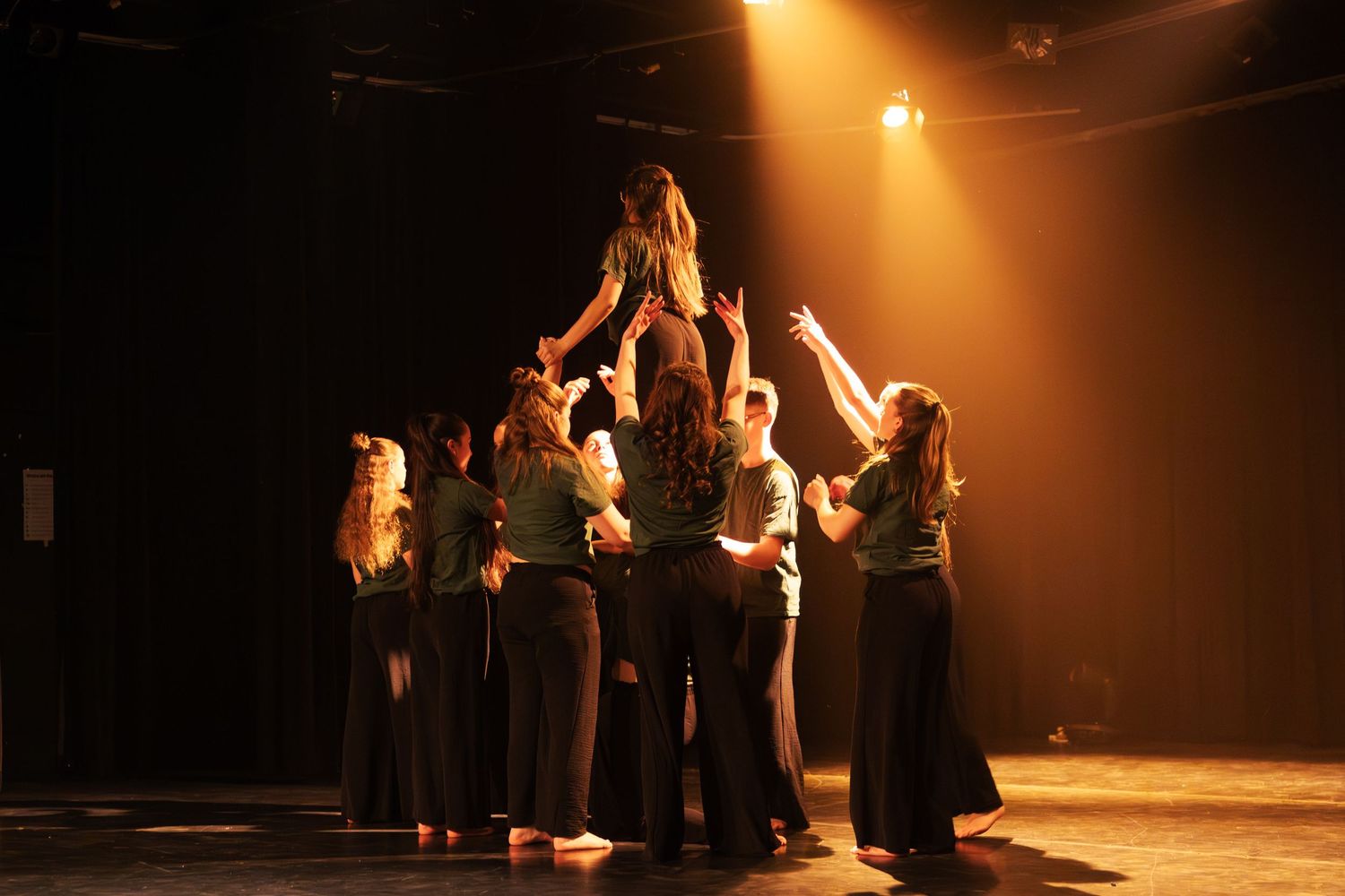 Dance ensemble lifts a performer overhead in a dramatic finale under golden stage lighting.