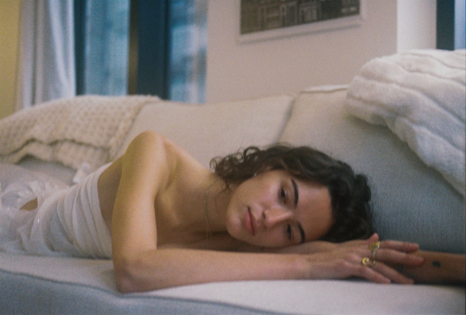 Young woman with curly hair resting on a couch wearing a white top.