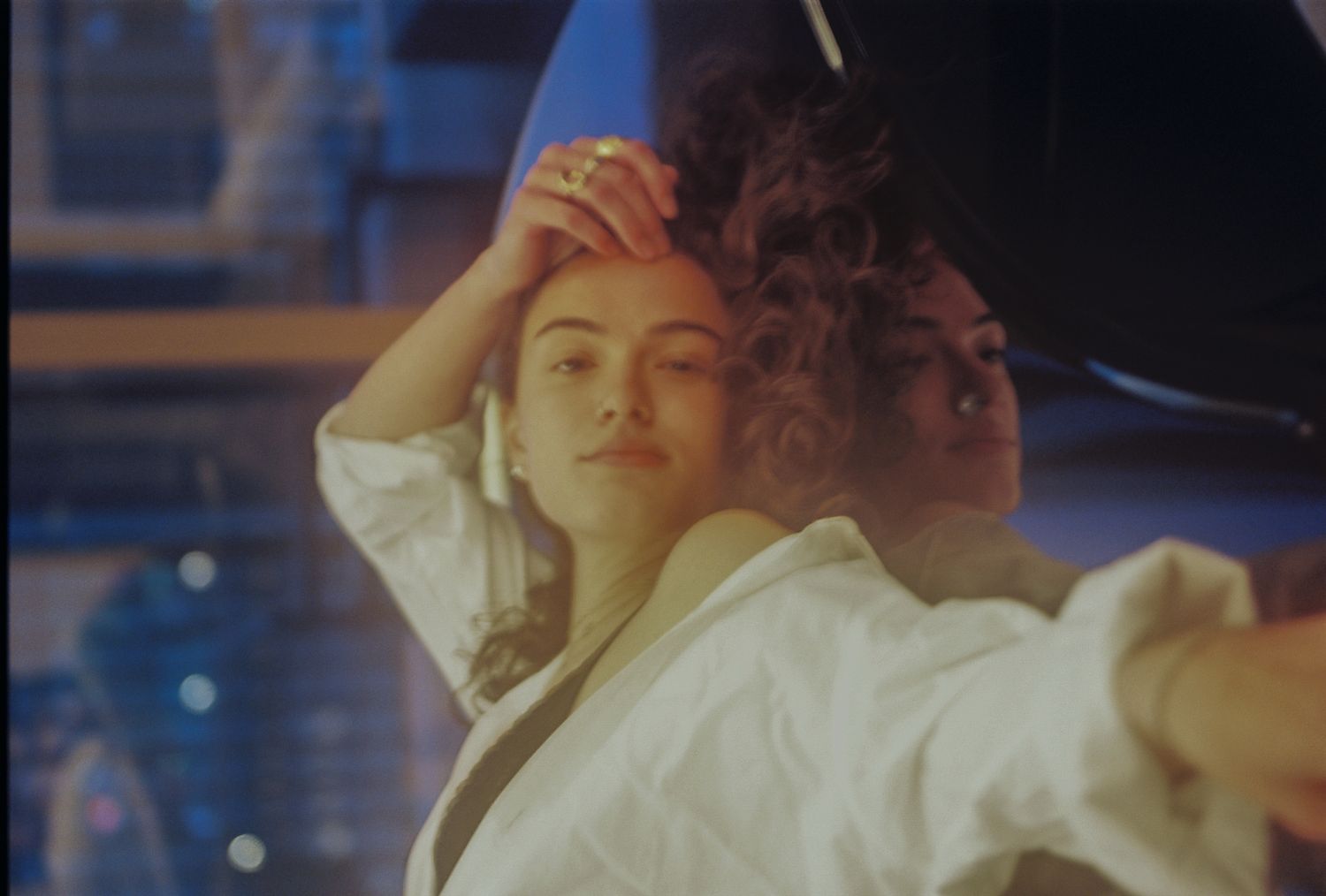 Two women posing together in soft cinematic lighting, one in a white jacket with curly hair.