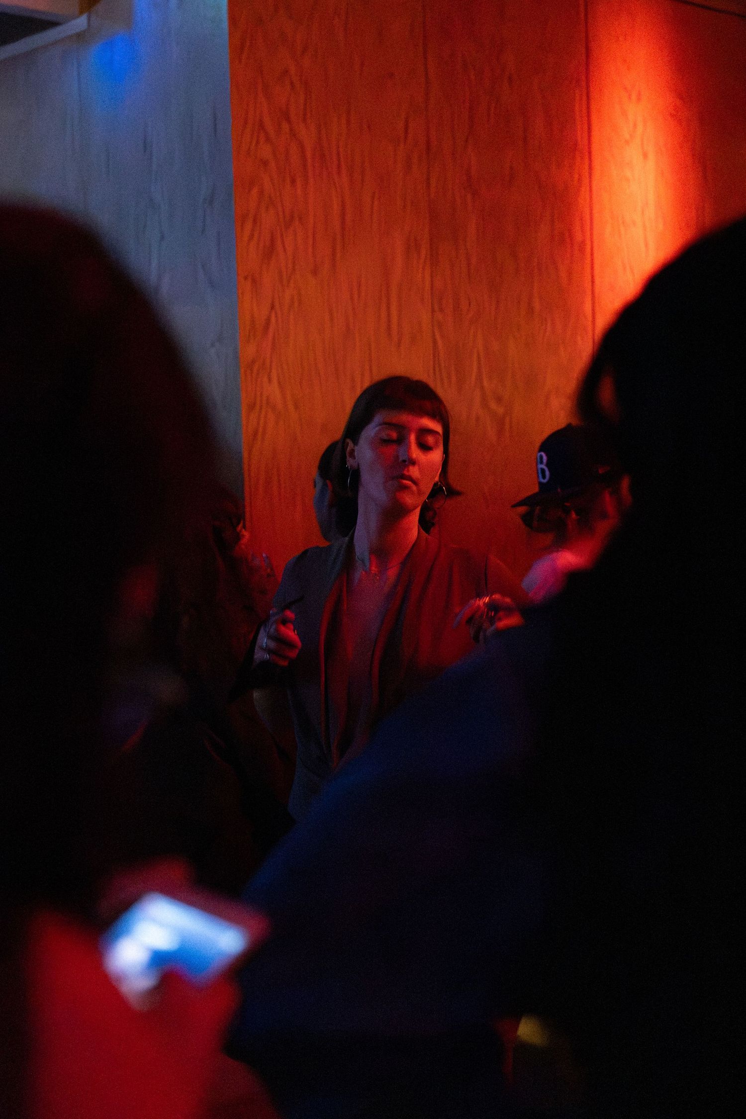 Person stands against a wooden wall bathed in red and blue light.