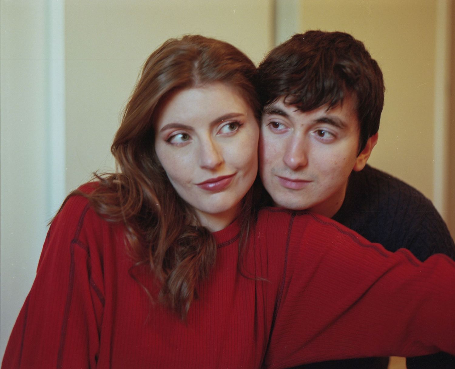A young couple in matching red outfits pose closely together, the woman leaning her head toward the man.