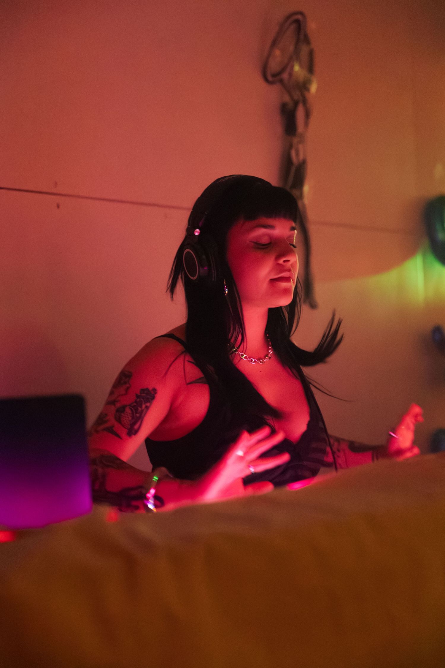 Tattooed woman with headphones DJing under red neon lights in a moody, atmospheric setting.
