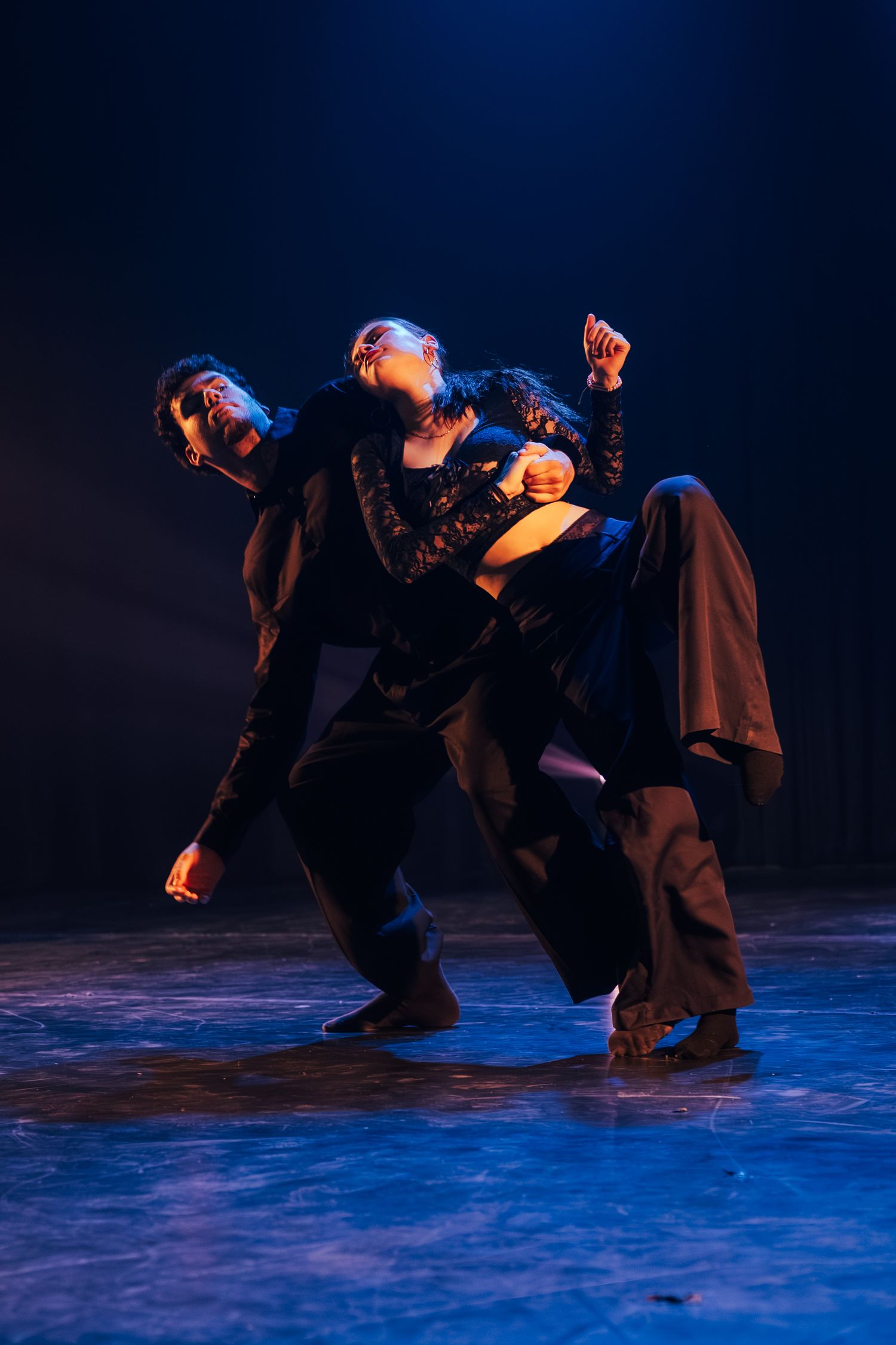 Two dancers performing dramatic contemporary dance routine under blue stage lighting.
