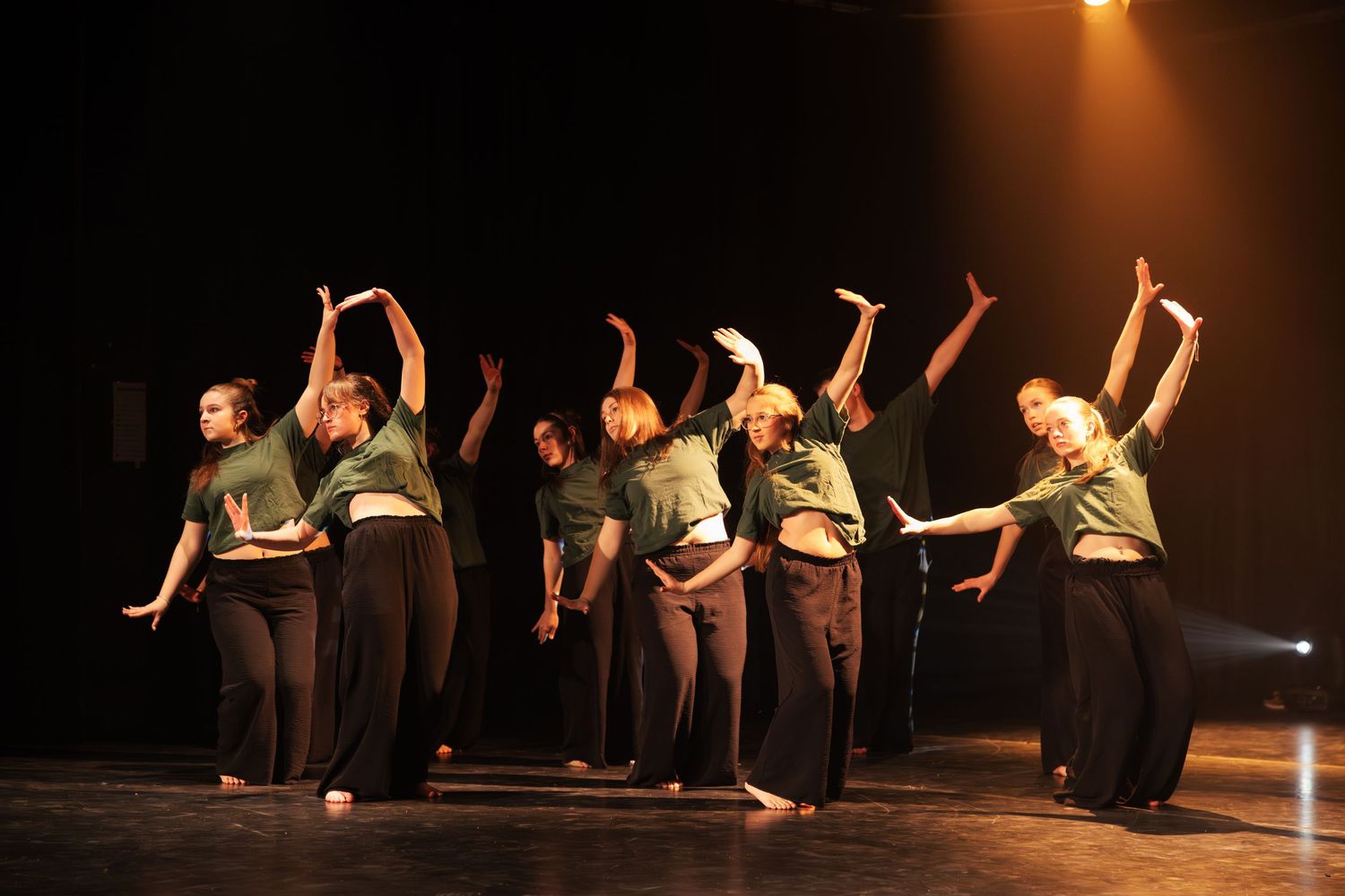 Group of dancers in matching green and black outfits perform choreography on a lit stage.