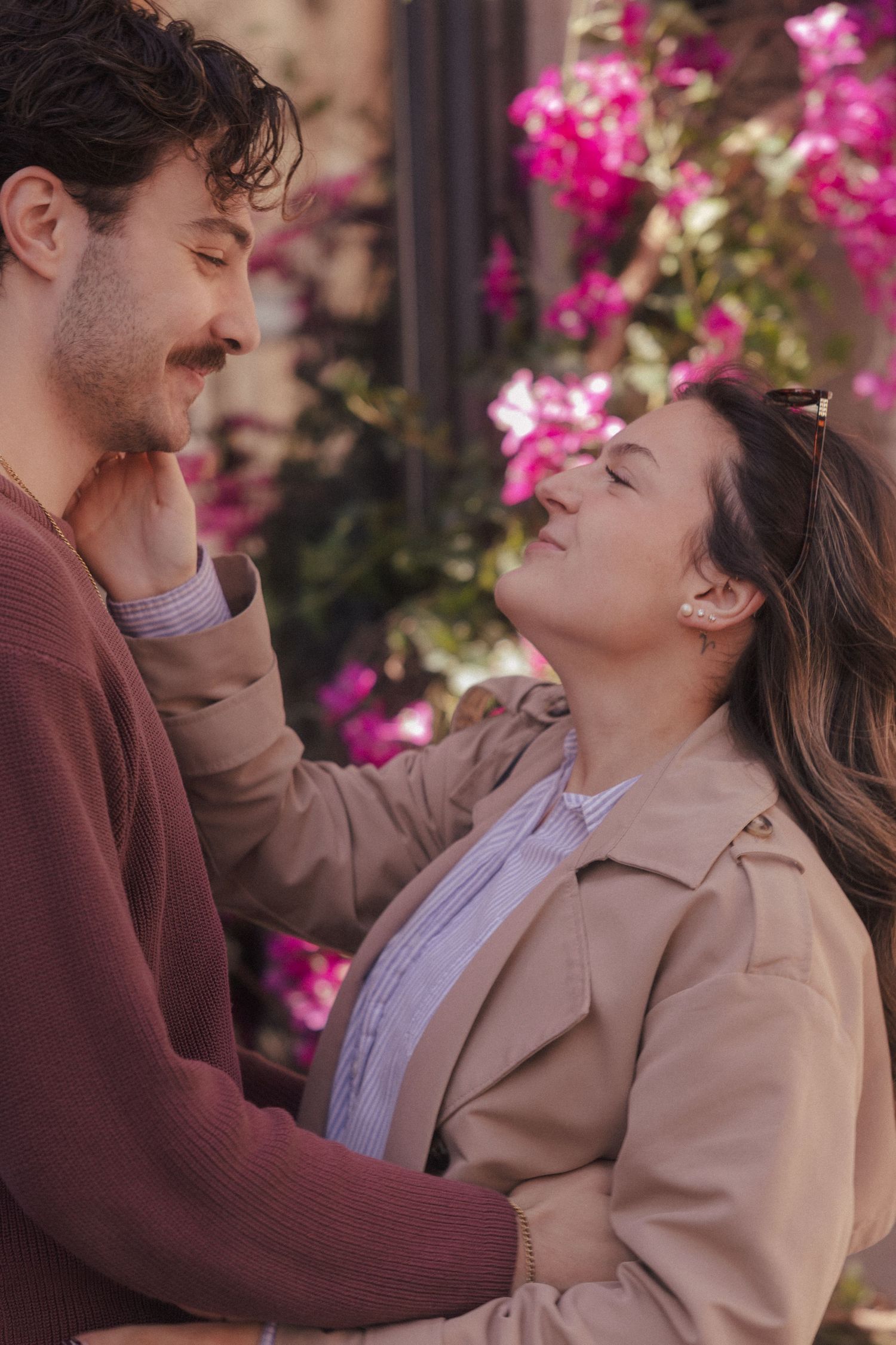 Romantic couple sharing tender moment outdoors surrounded by vibrant pink bougainvillea flowers.