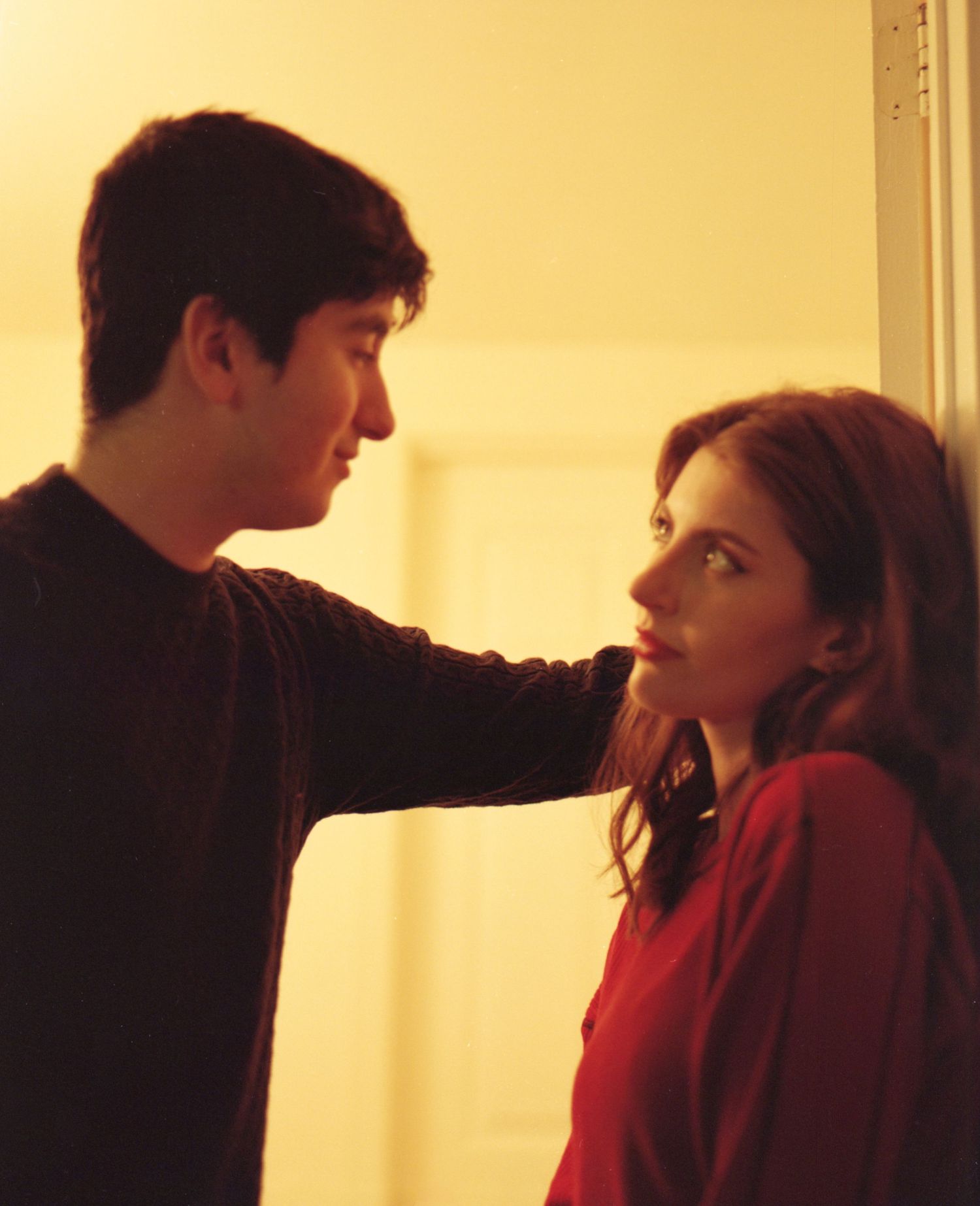 Young couple sharing an intimate moment leaning against a wall in warm golden light.