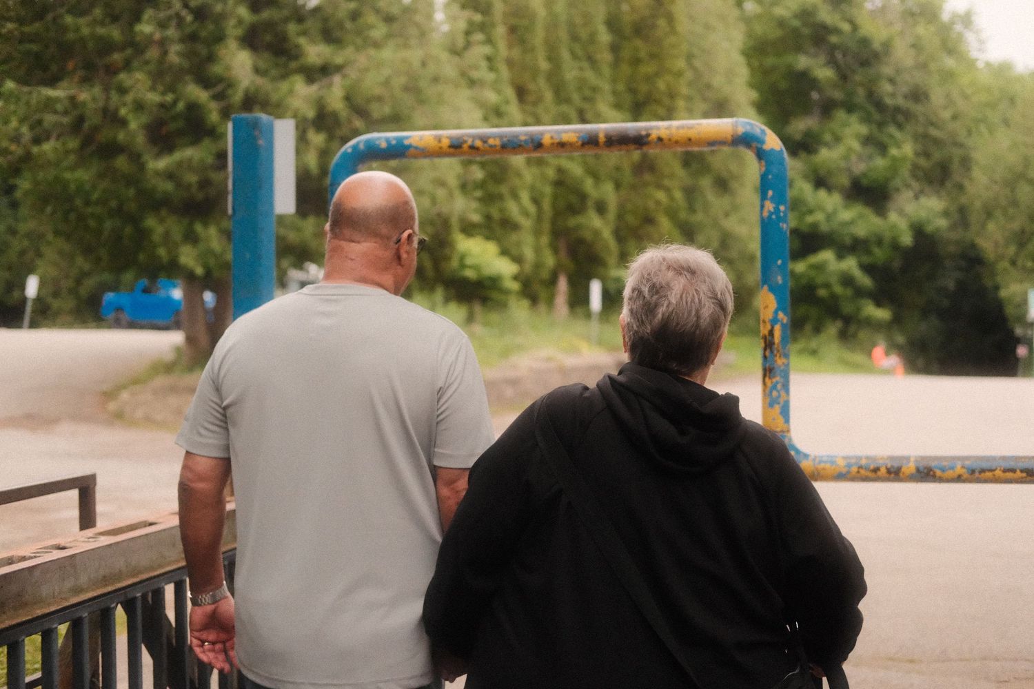 Two people viewed from behind leaning on a railing near a blue metal gate outdoors.
