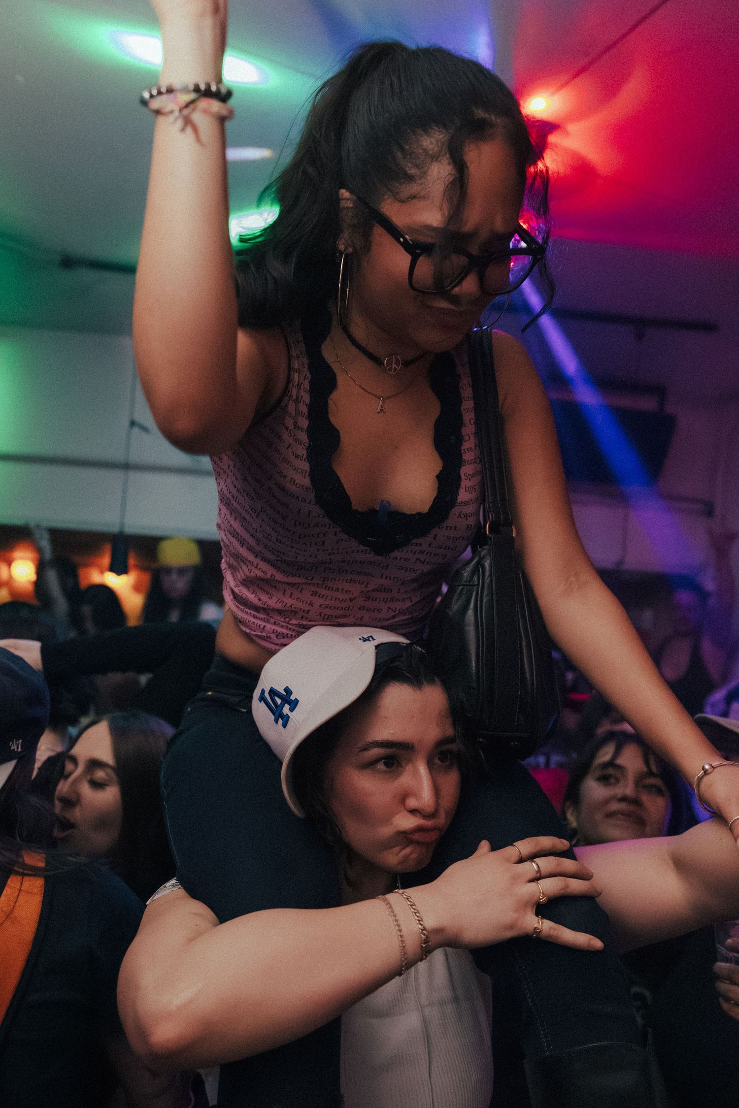 Woman sitting on shoulders of another person raises her hand in a crowded nightclub.