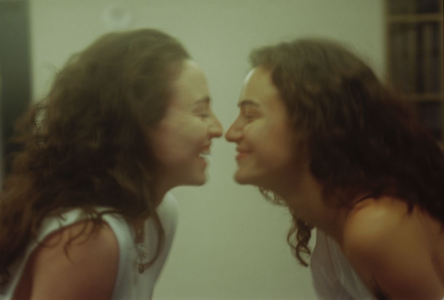 Two women with curly hair smiling and touching noses in a joyful close-up portrait.