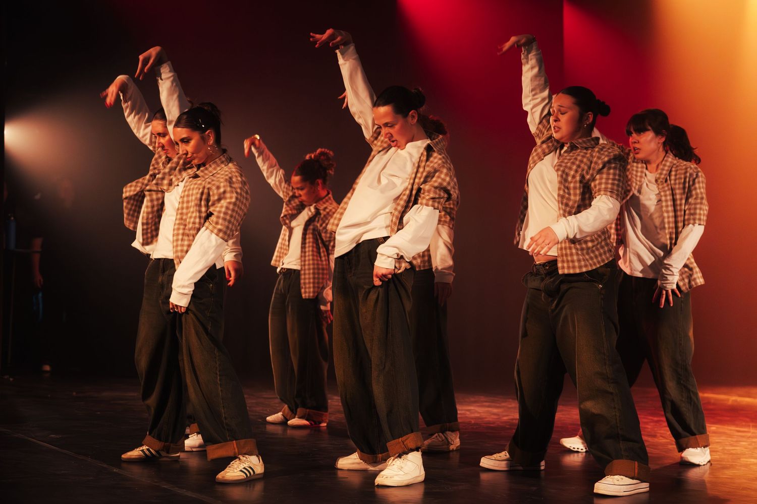 Hip-hop dance group performing synchronized routine in matching plaid shirts and baggy pants under warm stage lighting.