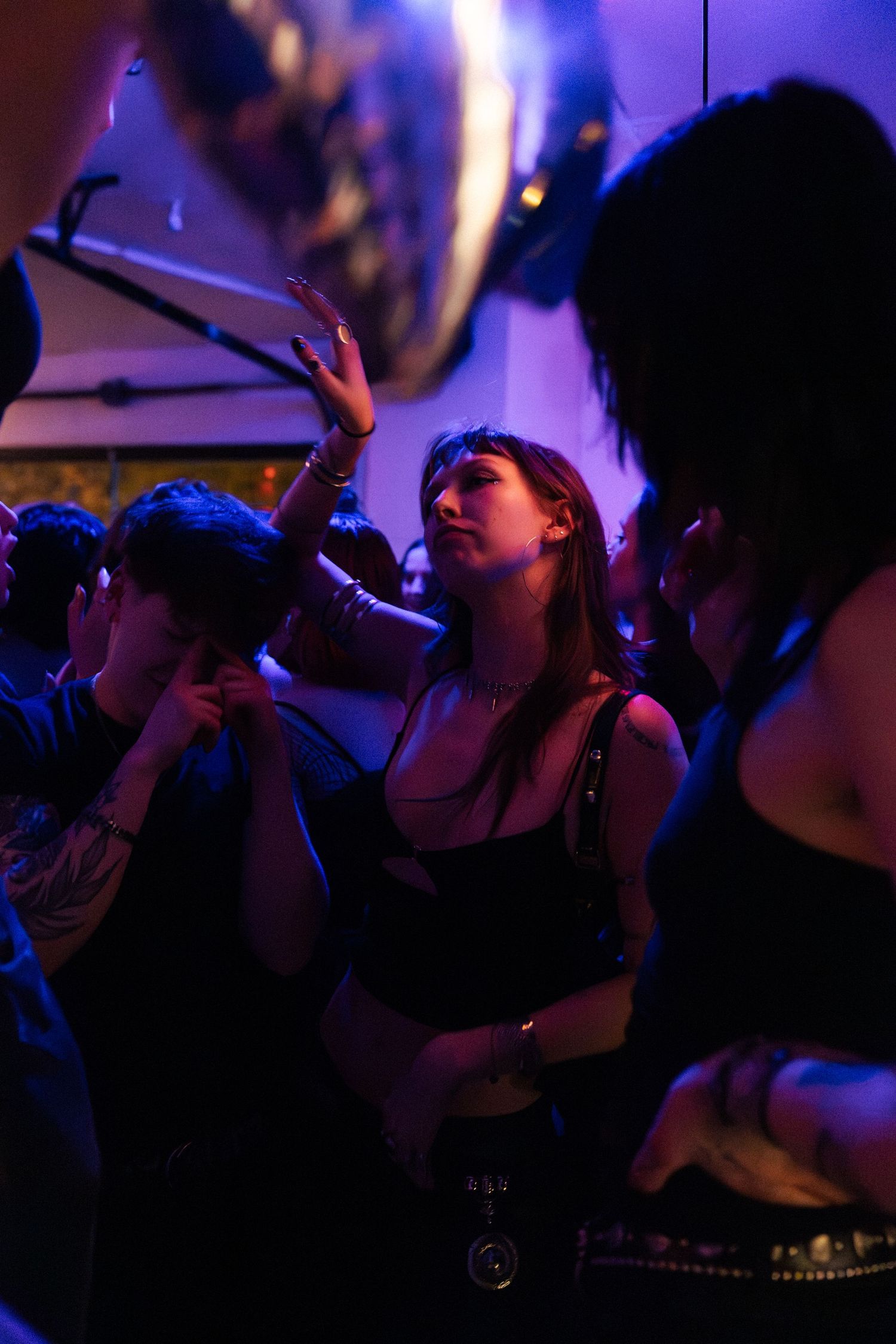 A young woman with raised hand dances in purple and blue nightclub lighting.