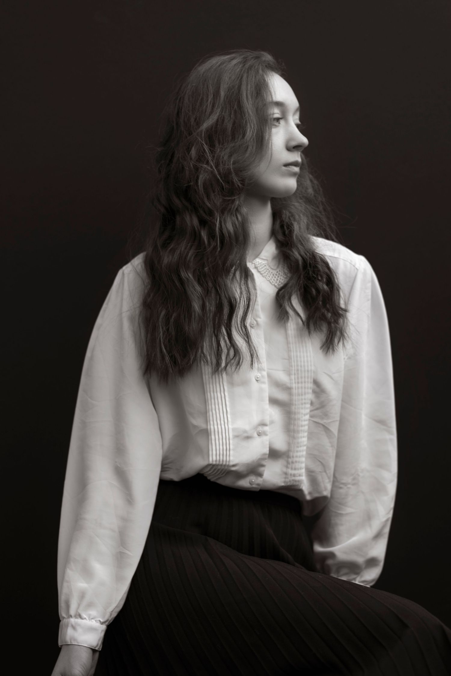 Elegant black and white portrait of a young woman in a white button-up shirt and black skirt looking sideways.