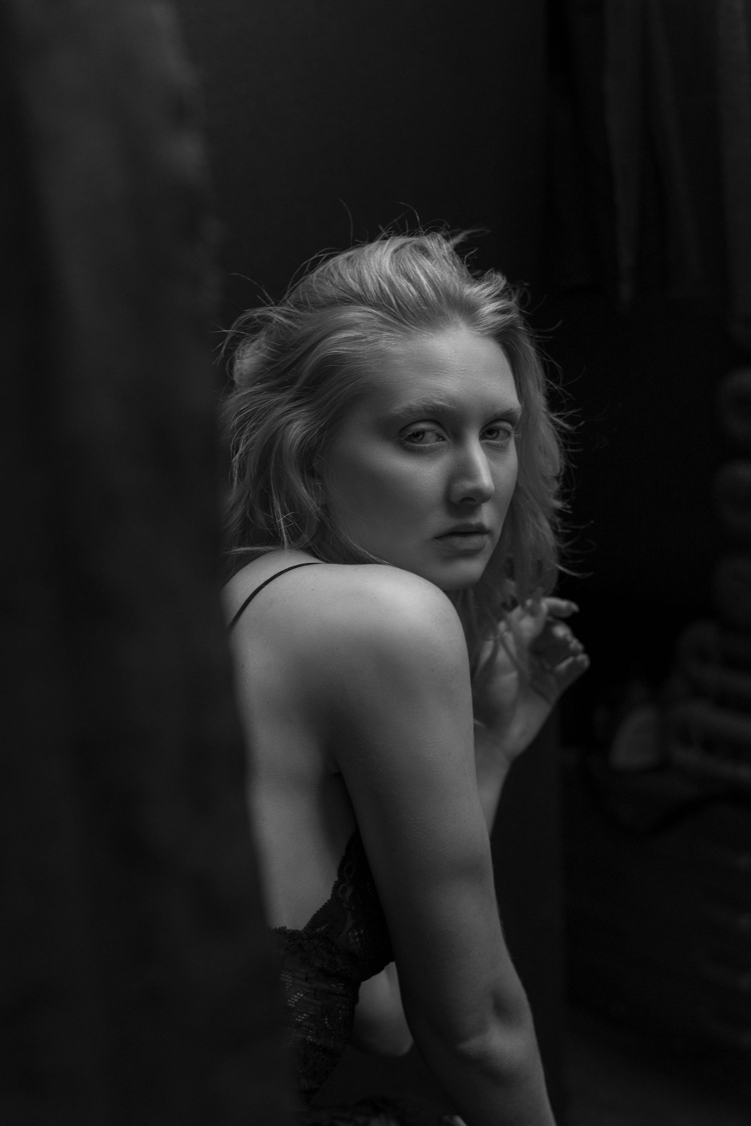 Blonde woman in black dress glancing over shoulder in dramatic dark black and white portrait.