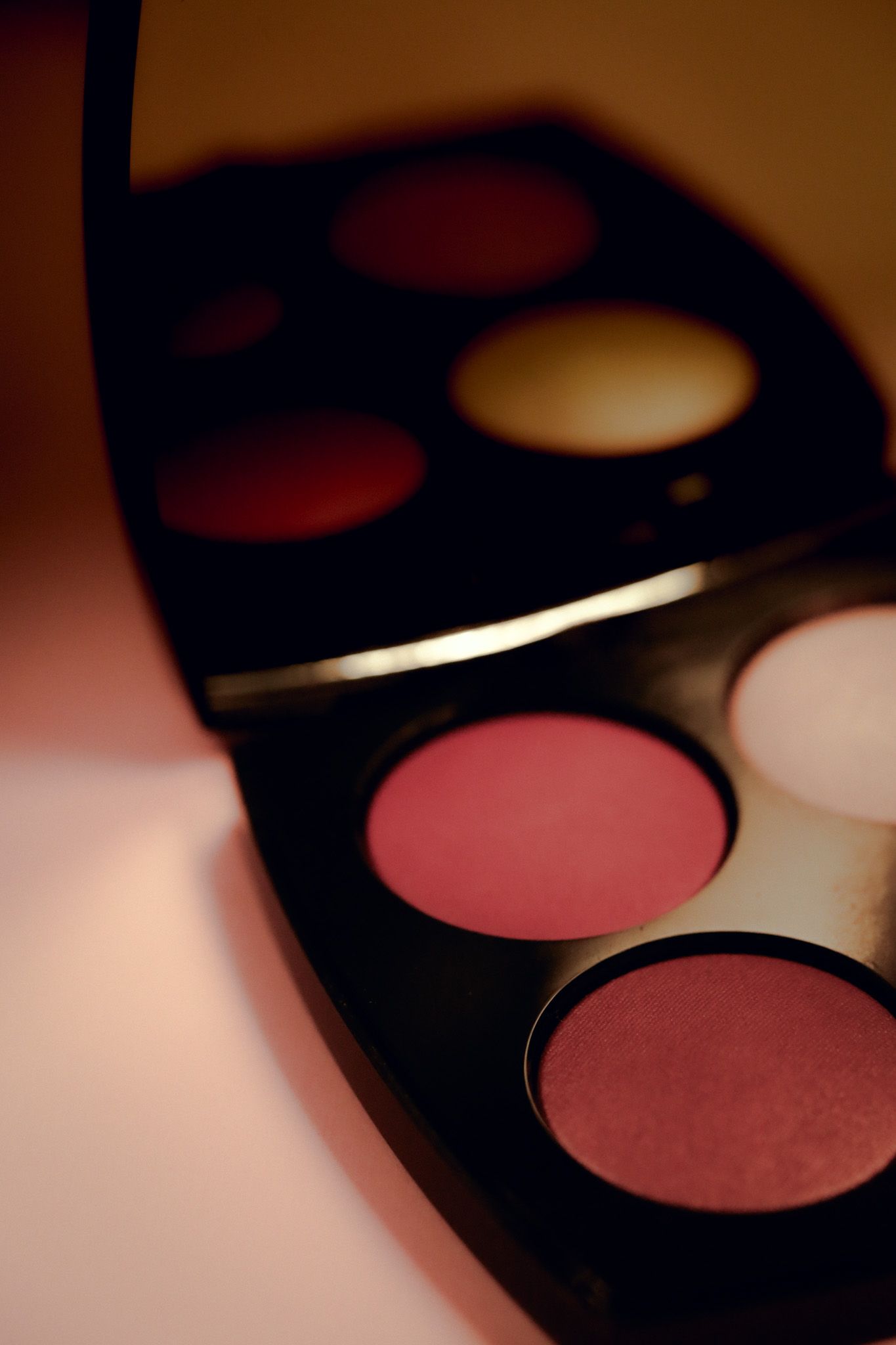 Close-up of an open black makeup palette with pink blush and eyeshadow shades in warm tones.