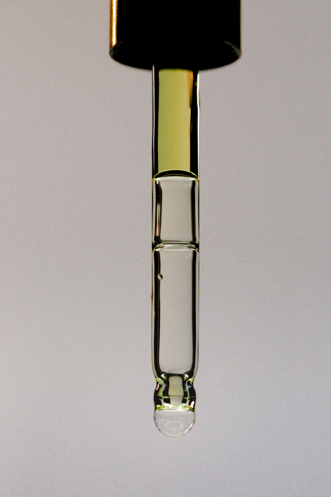 Close-up of a glass dropper pipette with golden serum and a single drop forming at the tip.