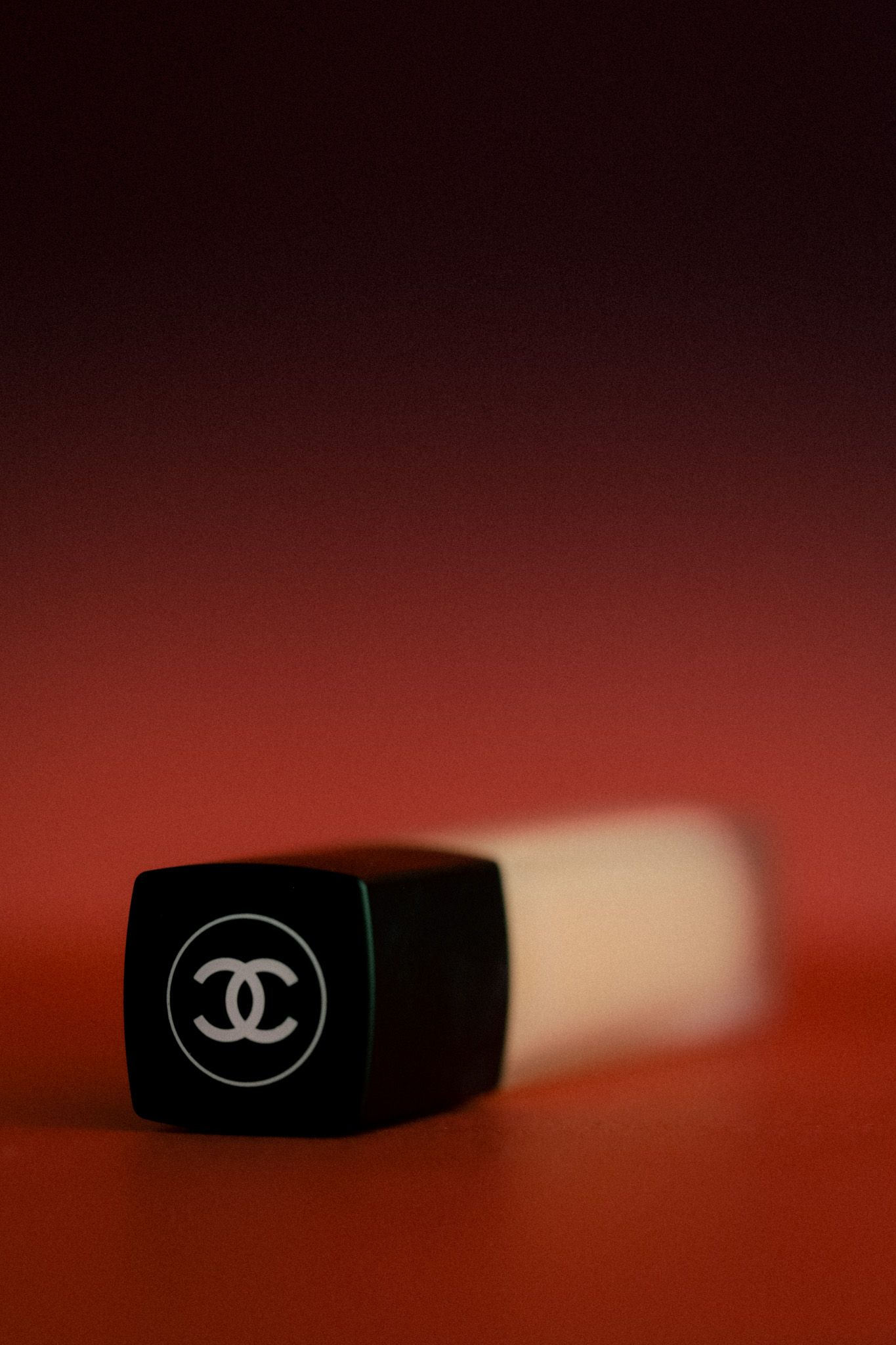 Chanel lipstick with iconic CC logo on black cap against a rich red background.
