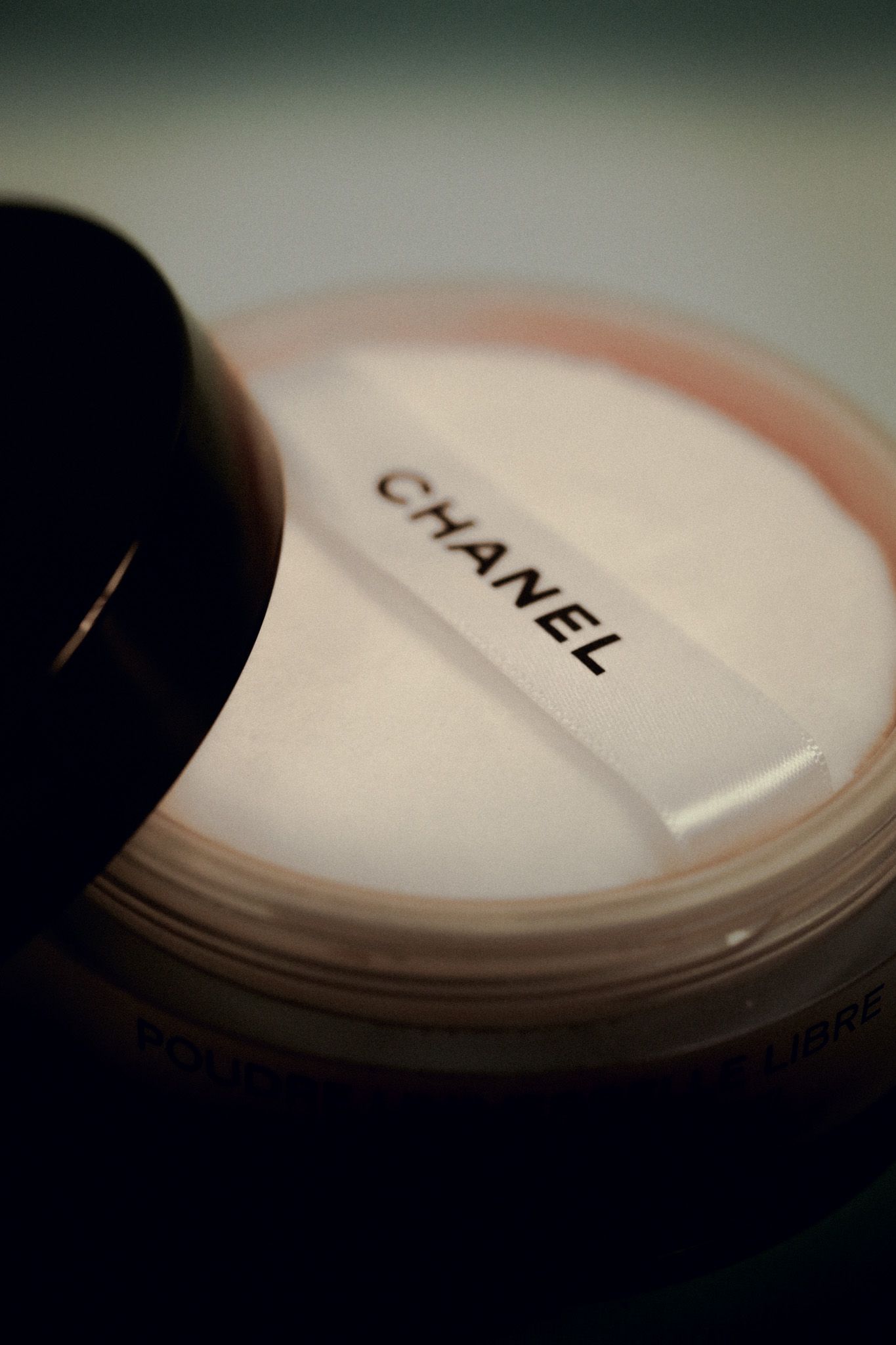 Chanel loose face powder in an open jar with a white velvet puff applicator on dark background.