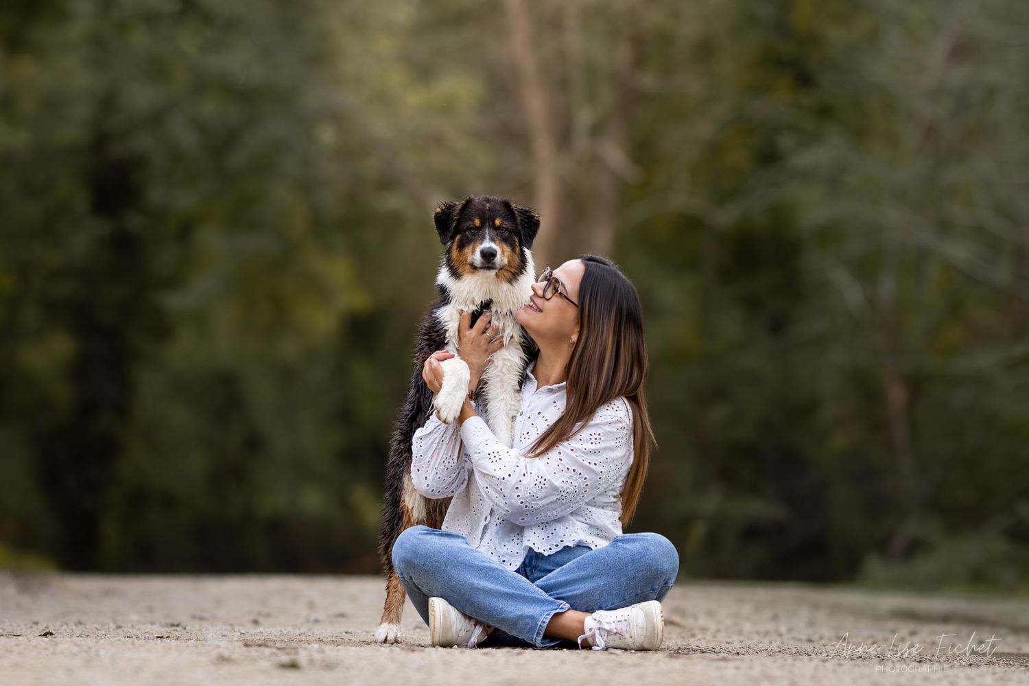Woman sitting on a dirt path holding an Bernese Mountain Dog puppy in a lush green forest setting.